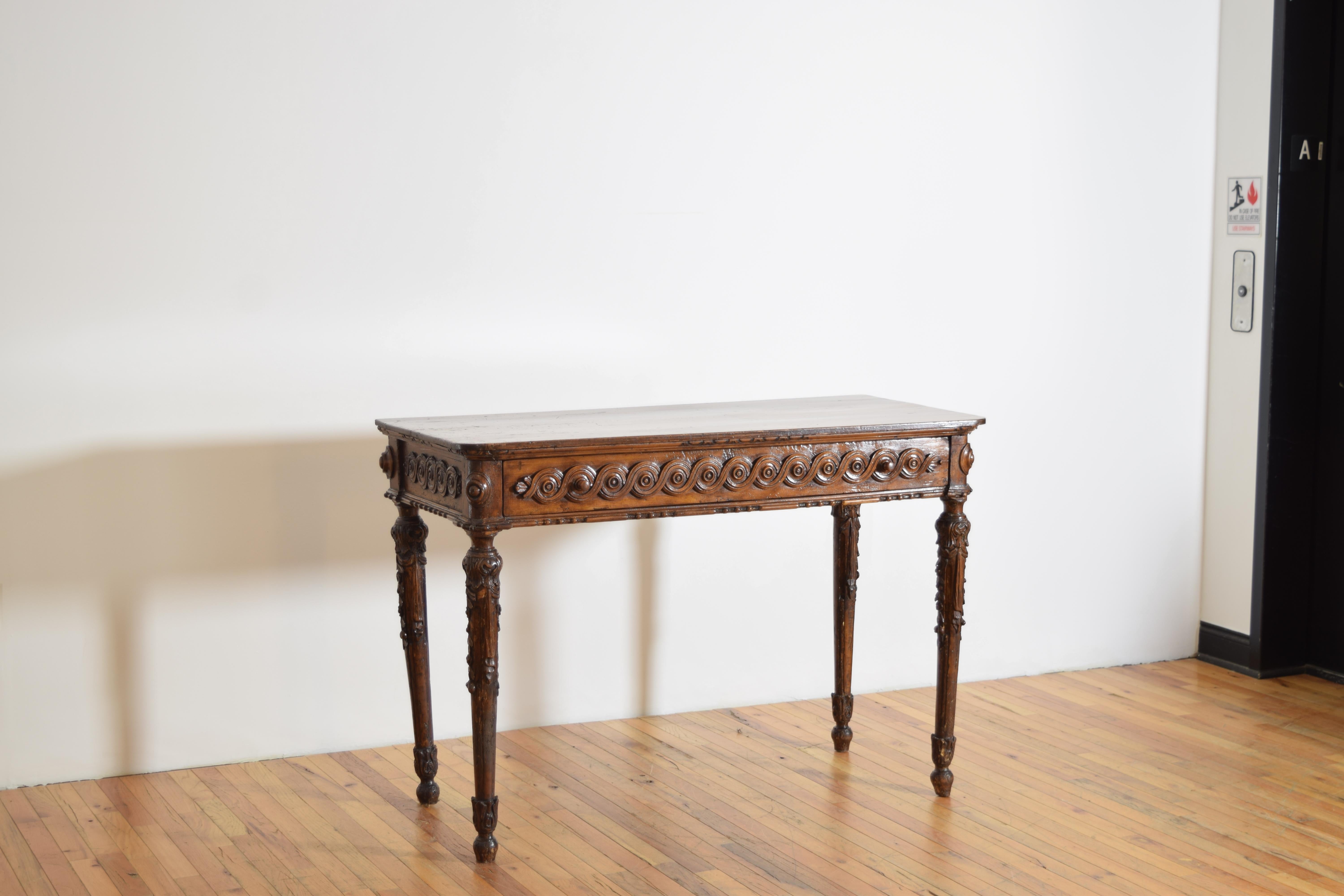 having a rectangular top with rounded front corners above an apron that is precisely carved with continuous roundels, raised on round tapering legs with carved leafage and hanging vines, later top