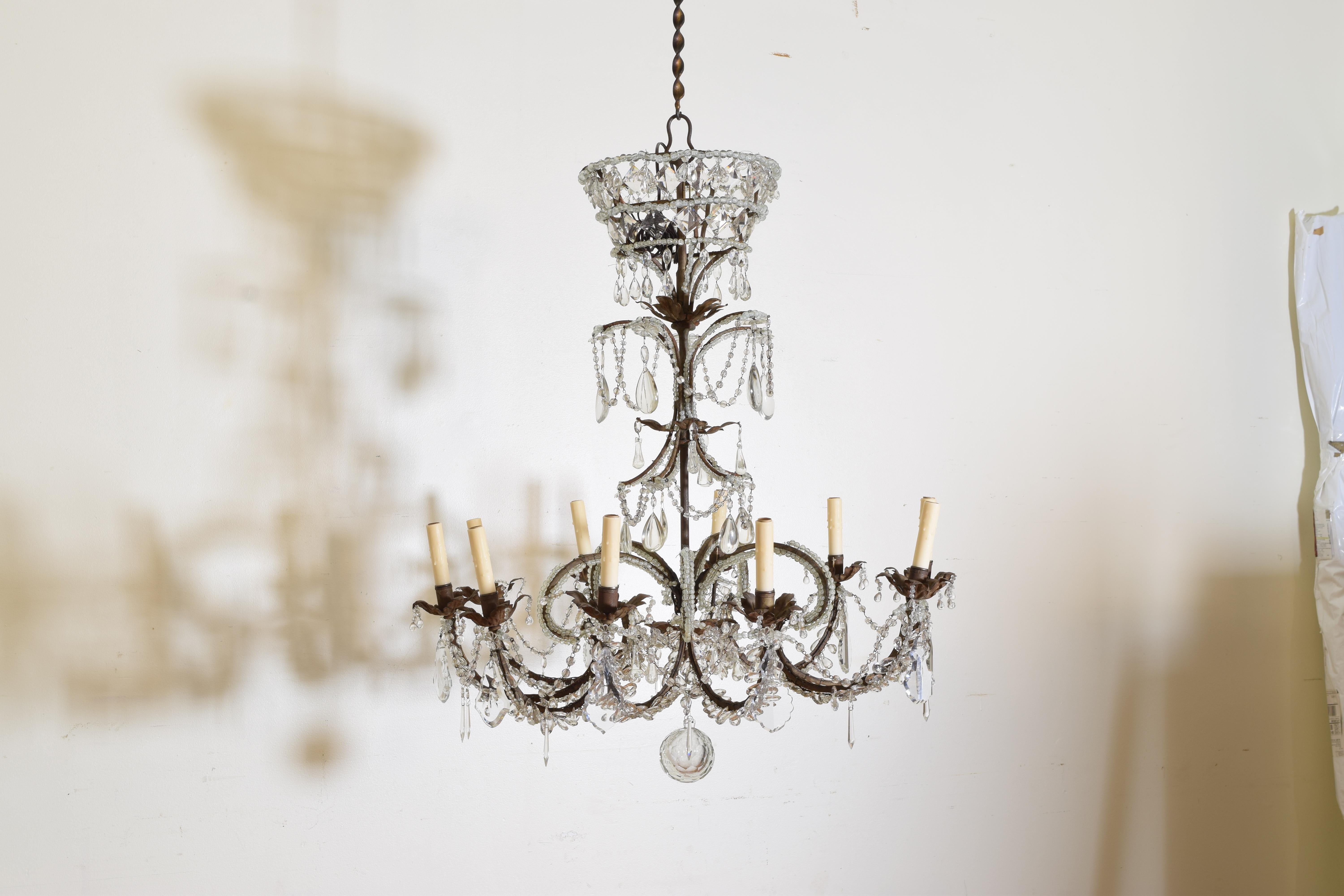 Uniquely crafted in the Rococo style this chandelier is constructed of iron with scrolled arms with metal bobeches retaining some gilding, the scrolled arms fitted with glass prisms and connected by glass bead chains, the top of graduated crown or