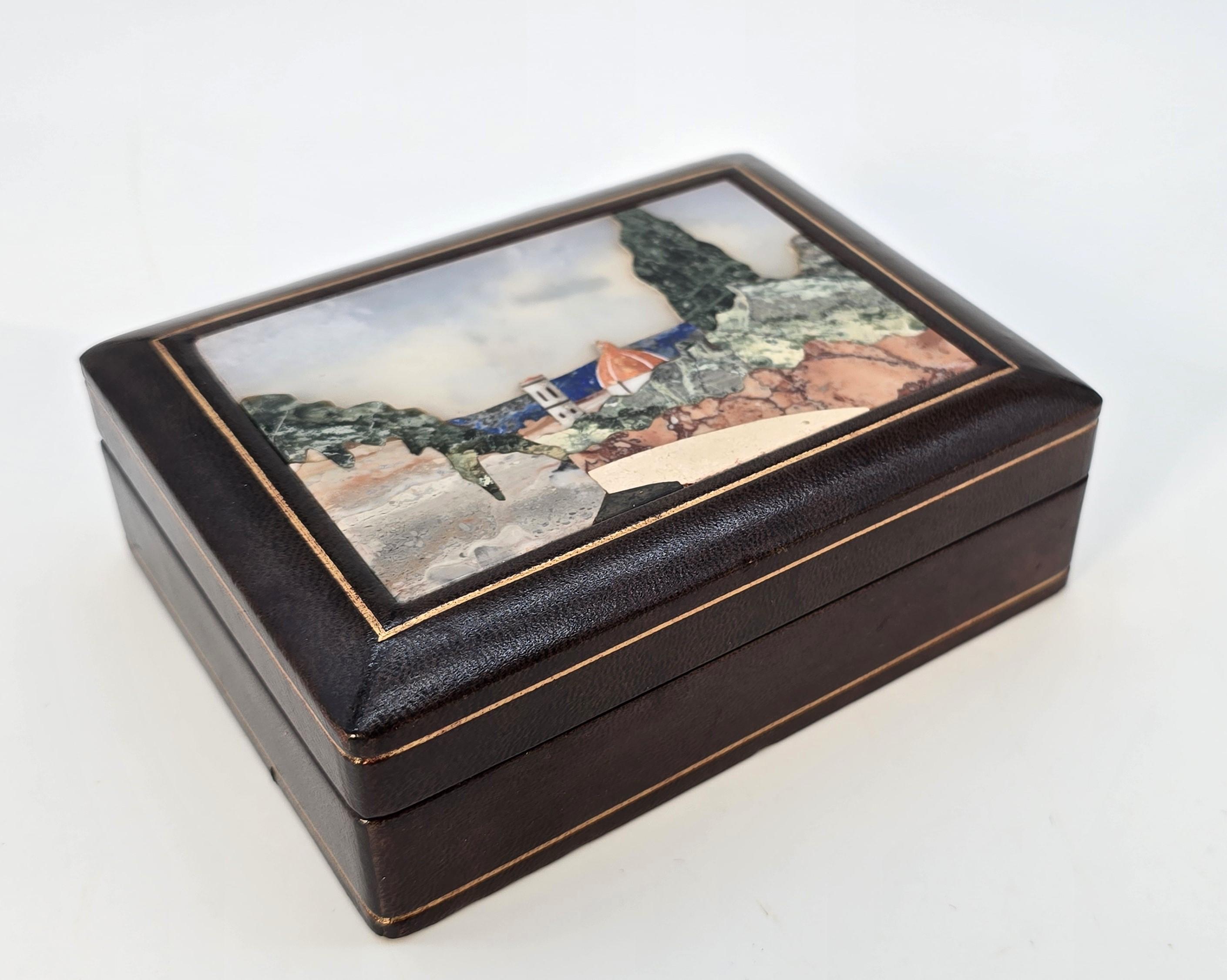 This superb Italian box dates to circa 1930. It is made from wood, and the exterior is covered in fine leather, which is panelled with gilt tooling.

The top of the box is inset with a pietra dura panel which shows a wonderfully detailed landscape