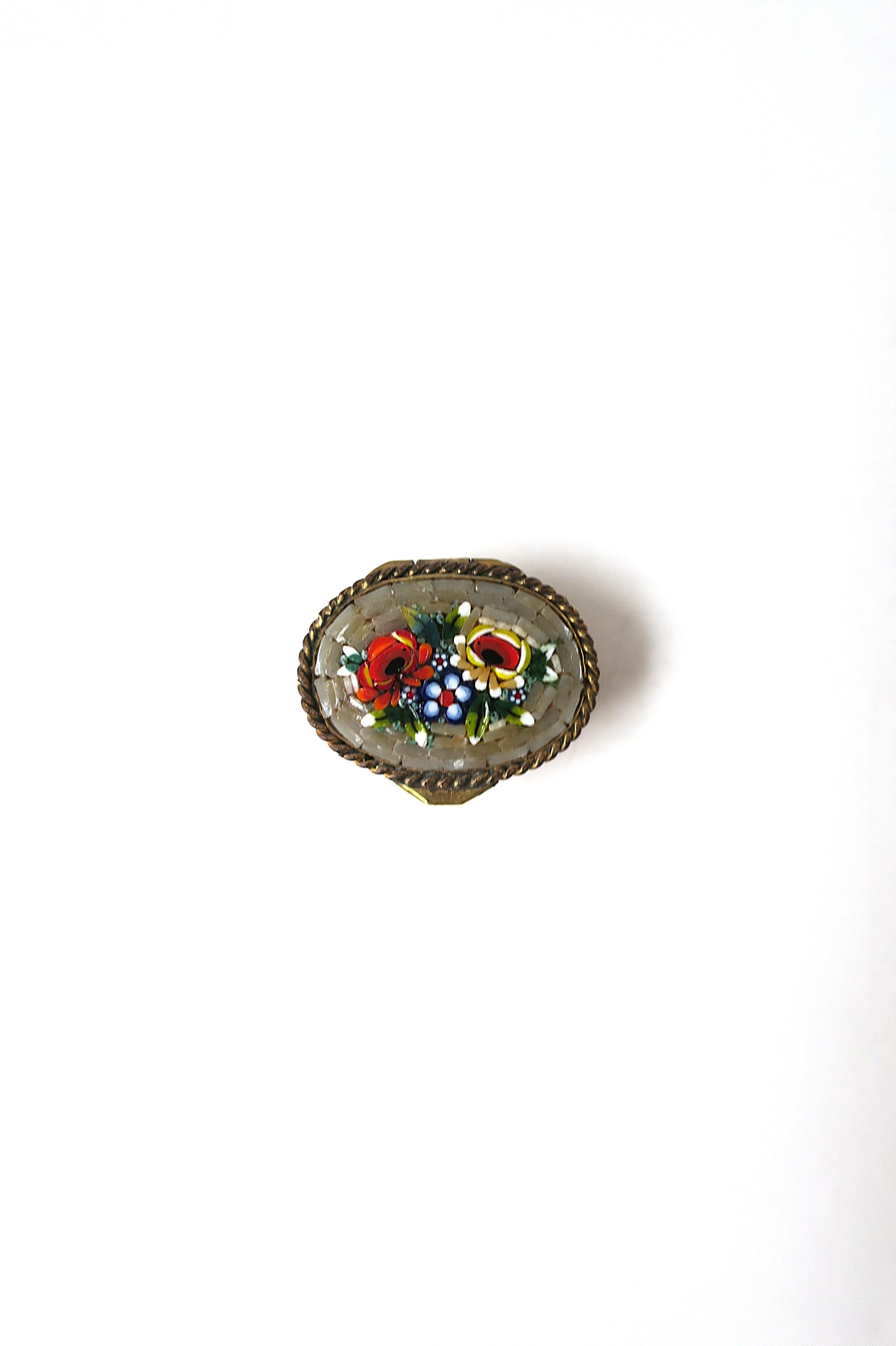 A beautiful oval Italian brass pill box with an inlayed floral glass micro mosaic millefiori design and twisted rope top lid, finished with a brass exterior repoussé design of flowers, leaves and grapes, circa early to mid-20th century, Italy. Box