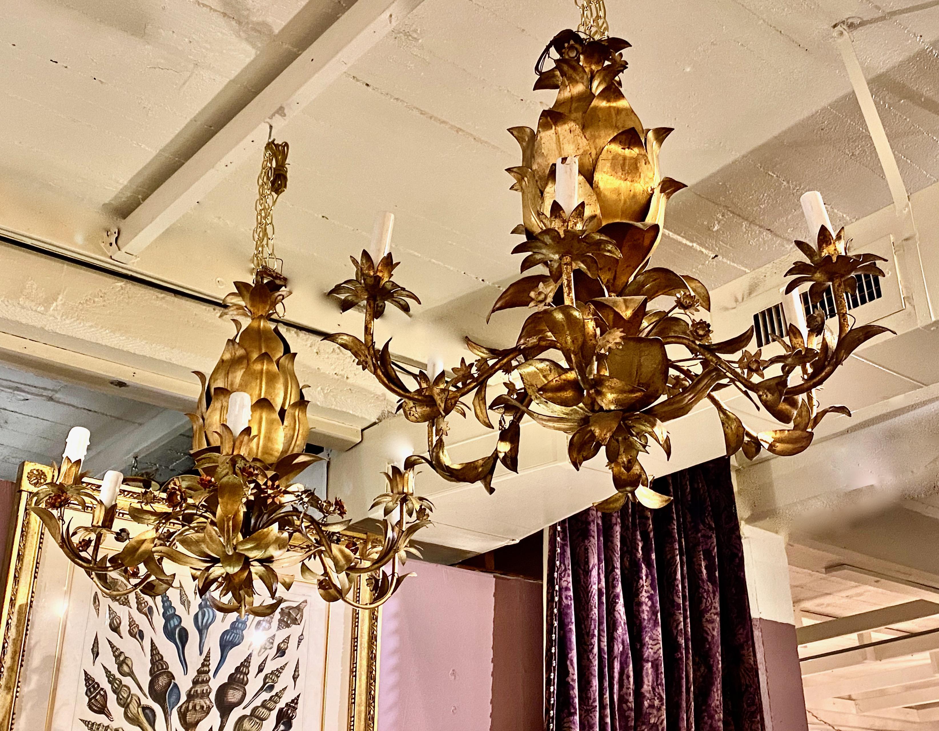 This is a fun near pair of c. 1960-1970 Italian gilt tole chandeliers in the form of a pineapple with painted tole flowers. The chandeliers are in very good overall condition with normal patination to the gold leaf. The wiring has been