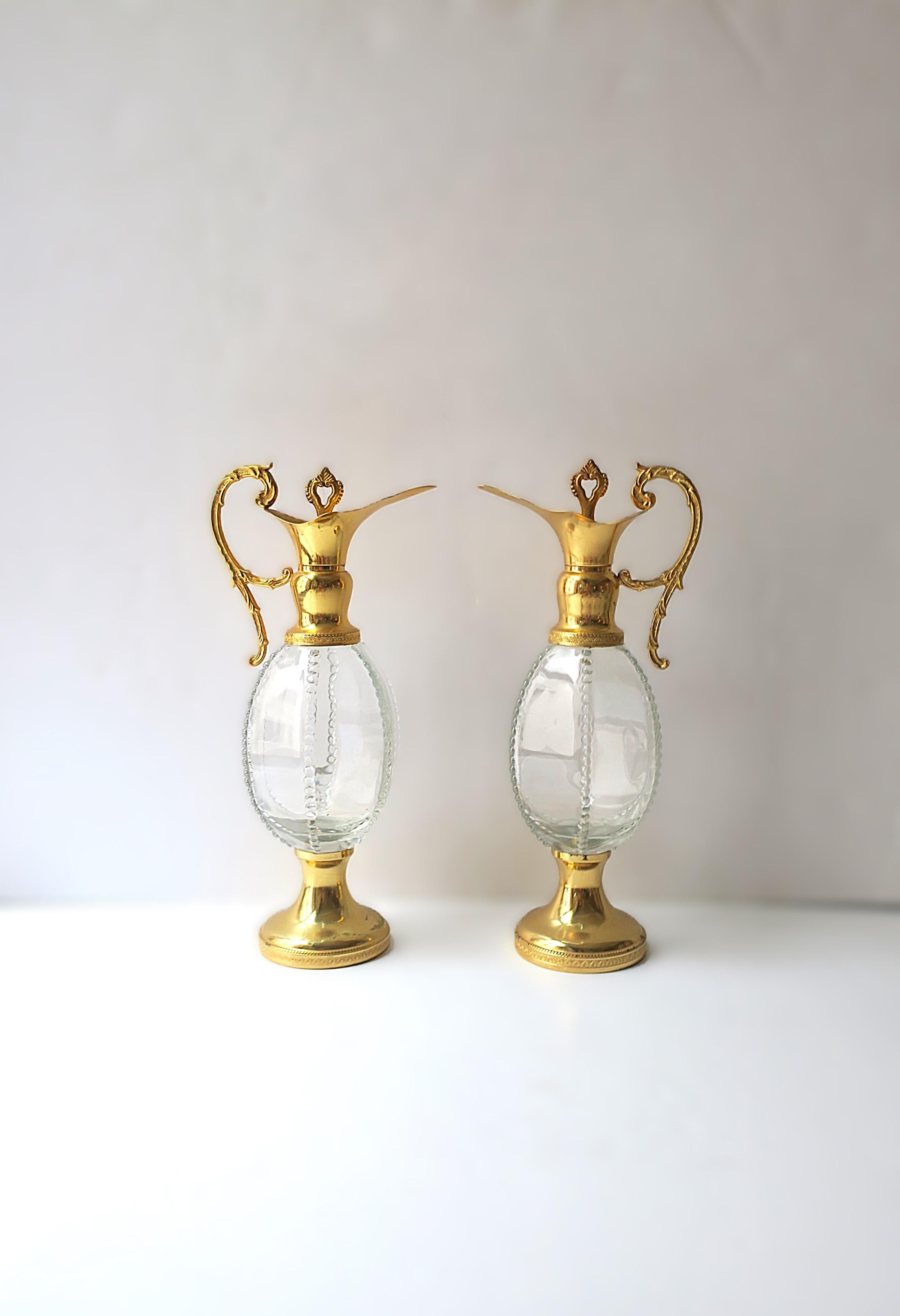 Se venden por pares. Juego/par italiano de jarras/copas de vino o licor de metal dorado o bronceado y cristal, hacia el siglo XX, Italia. Los cántaros/jarras tienen asas con volutas, tapones de metal dorado y corcho, centro de cristal en forma de