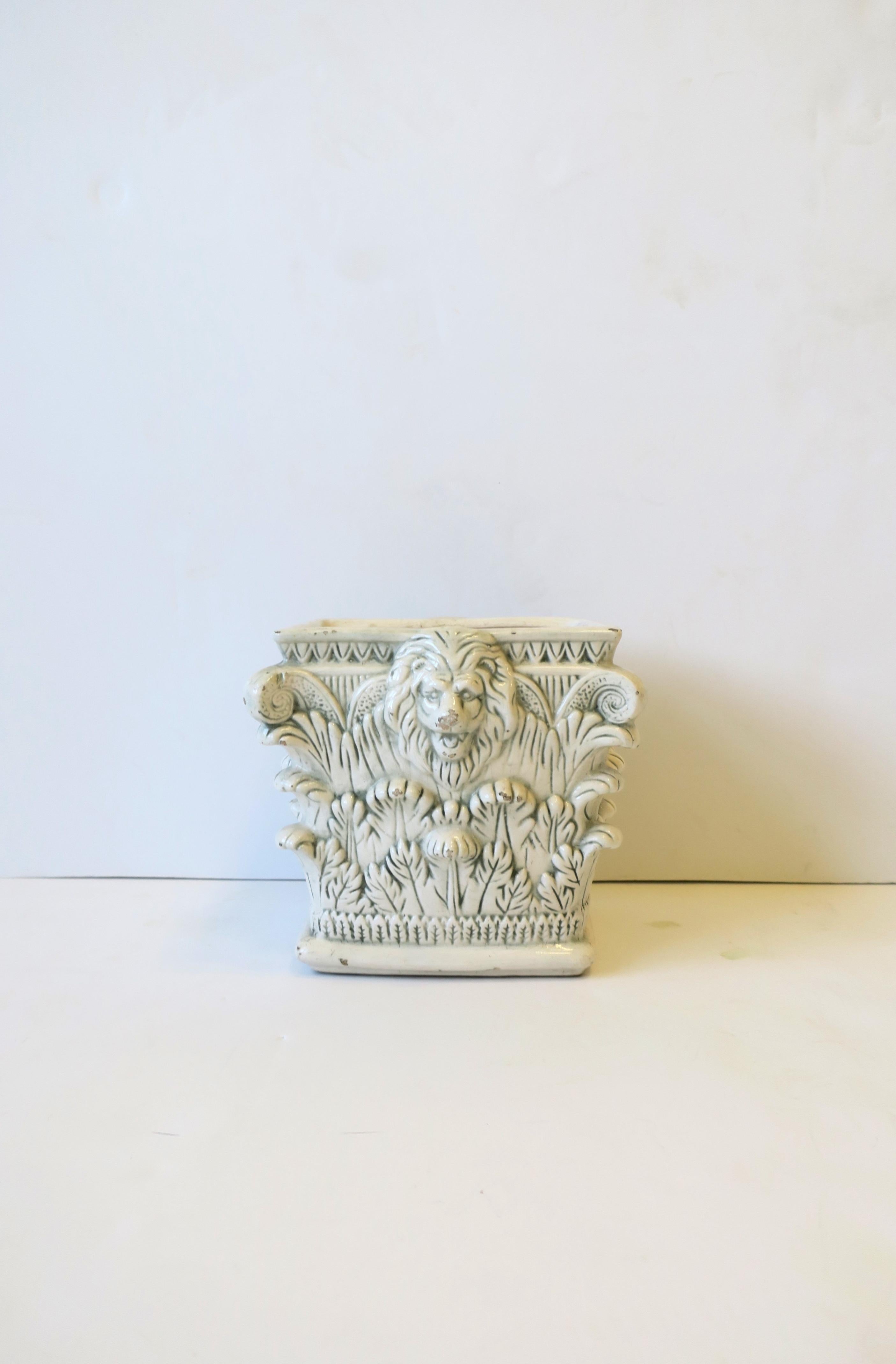 An Italian ceramic cachepot plant or flower-pot holder with lion-head design in Regency style, circa mid-20th century, Italy. Cachepot has a pillar-like design with lion head and acanthus leaf detail. Dimensions: 5.38