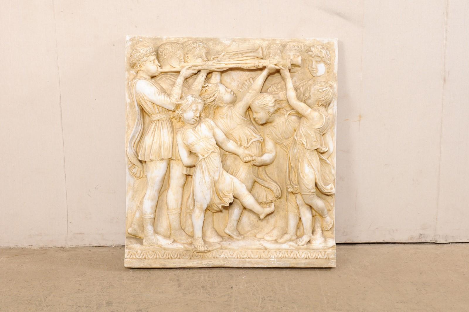 An Italian plaster wall sculpture relief plaque, in Roman figure theme, from the mid-20th century. This vintage art piece, created of plaster in relief, features younger children at play beneath three adolescent horn players, and their onlooking