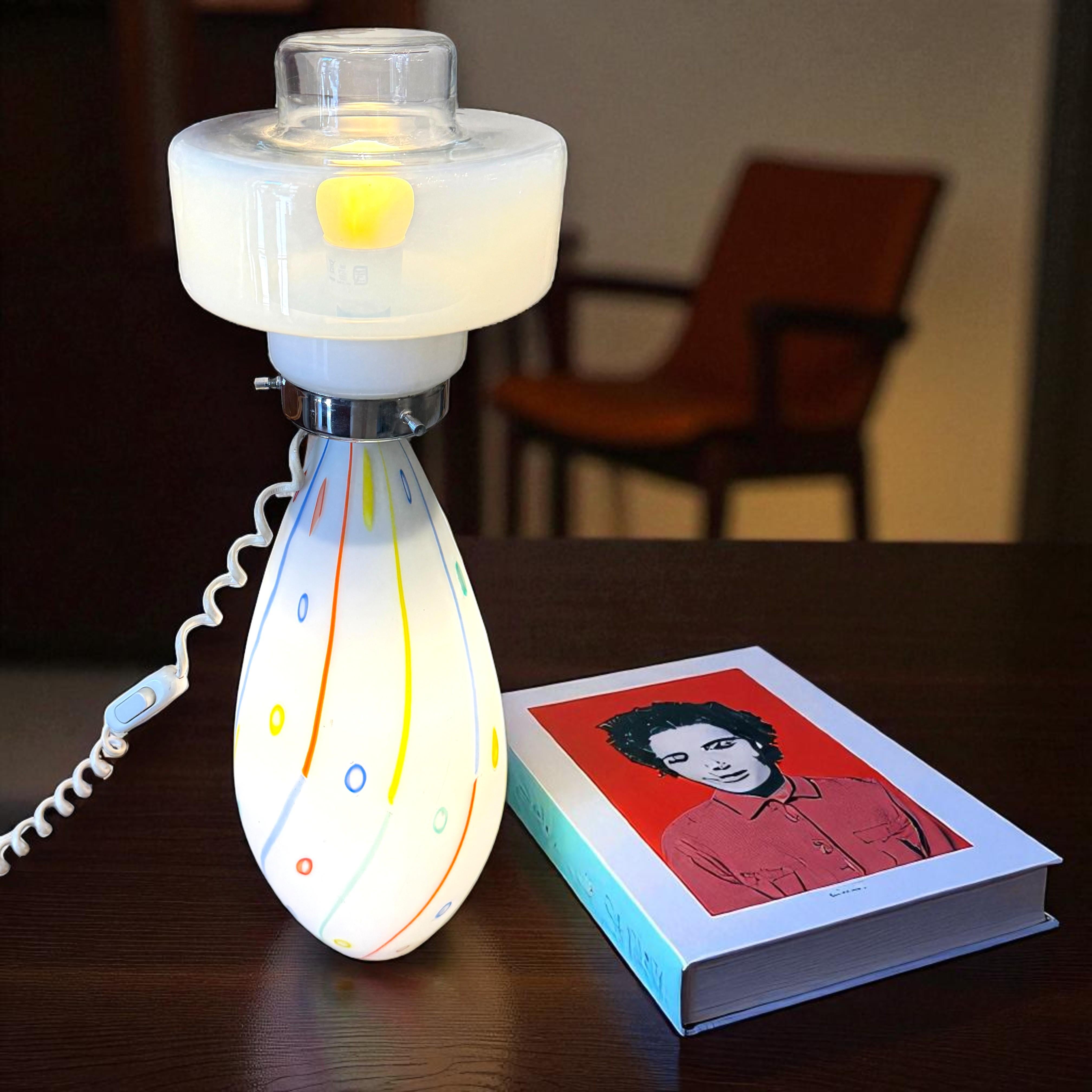 Apportez une touche poétique à votre intérieur avec cette lampe vintage italienne au charme intemporel, alliant verre de Murano et acier chromé dans une composition raffinée. Sa base en forme d'Amphora, ornée de motifs vibrants d'inspiration pop,