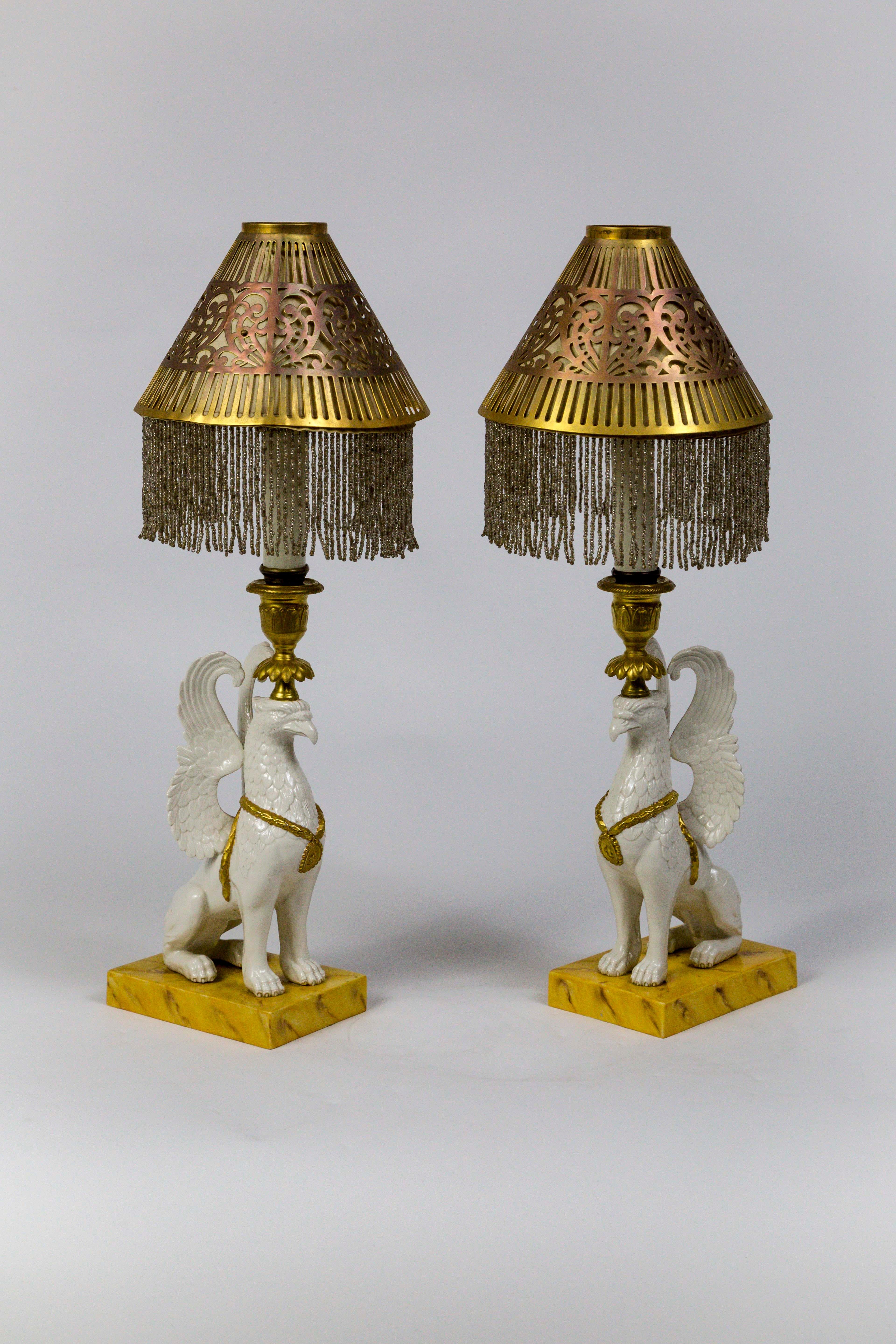 Finely crafted Porcellane d'Arte from Bassano del Grappa, Italy; hand painted, porcelain, urn crowned Griffin sculptures on gold painted bases as push-up candlesticks. Topped with brass shades with some copper tinting; empire shaped and trimmed with