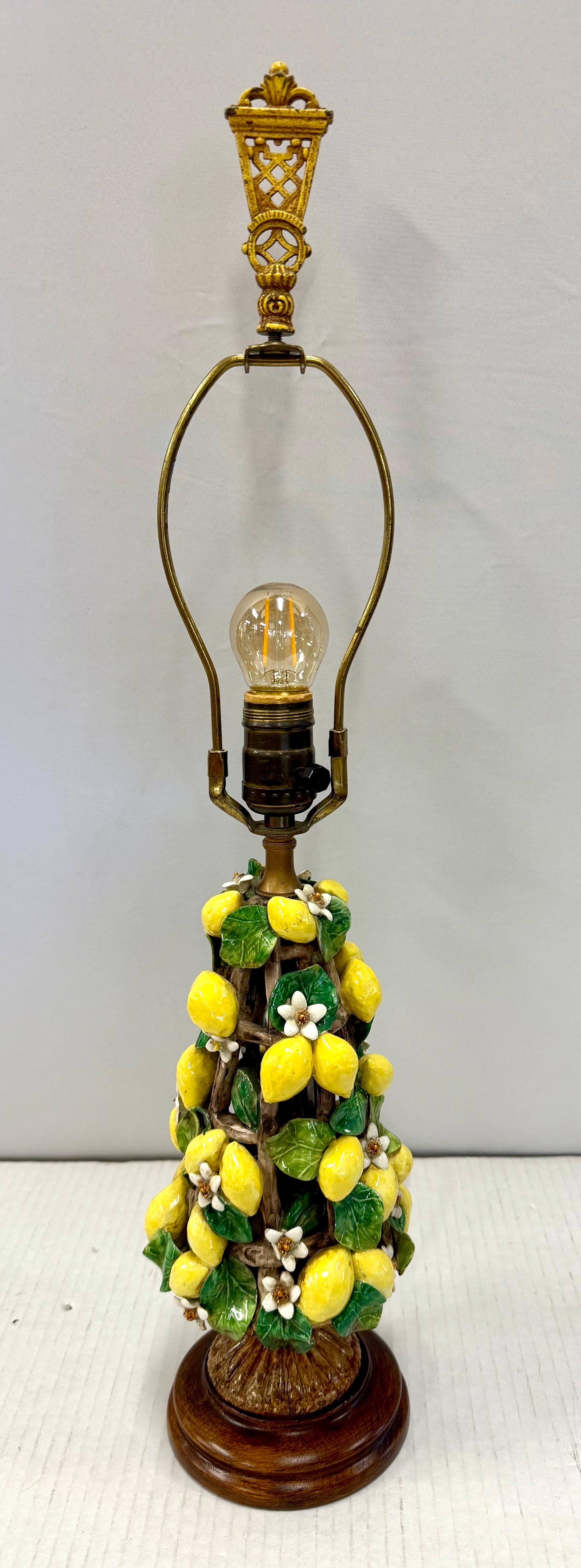 This delightful porcelain lemon topiary lamp has a hand painted base adorned with a vibrant cascade of lemons, lush green leaves, and delicate blossoms, arranged atop a wooden footed base.  Topped with a striking yellow tole shade and featuring