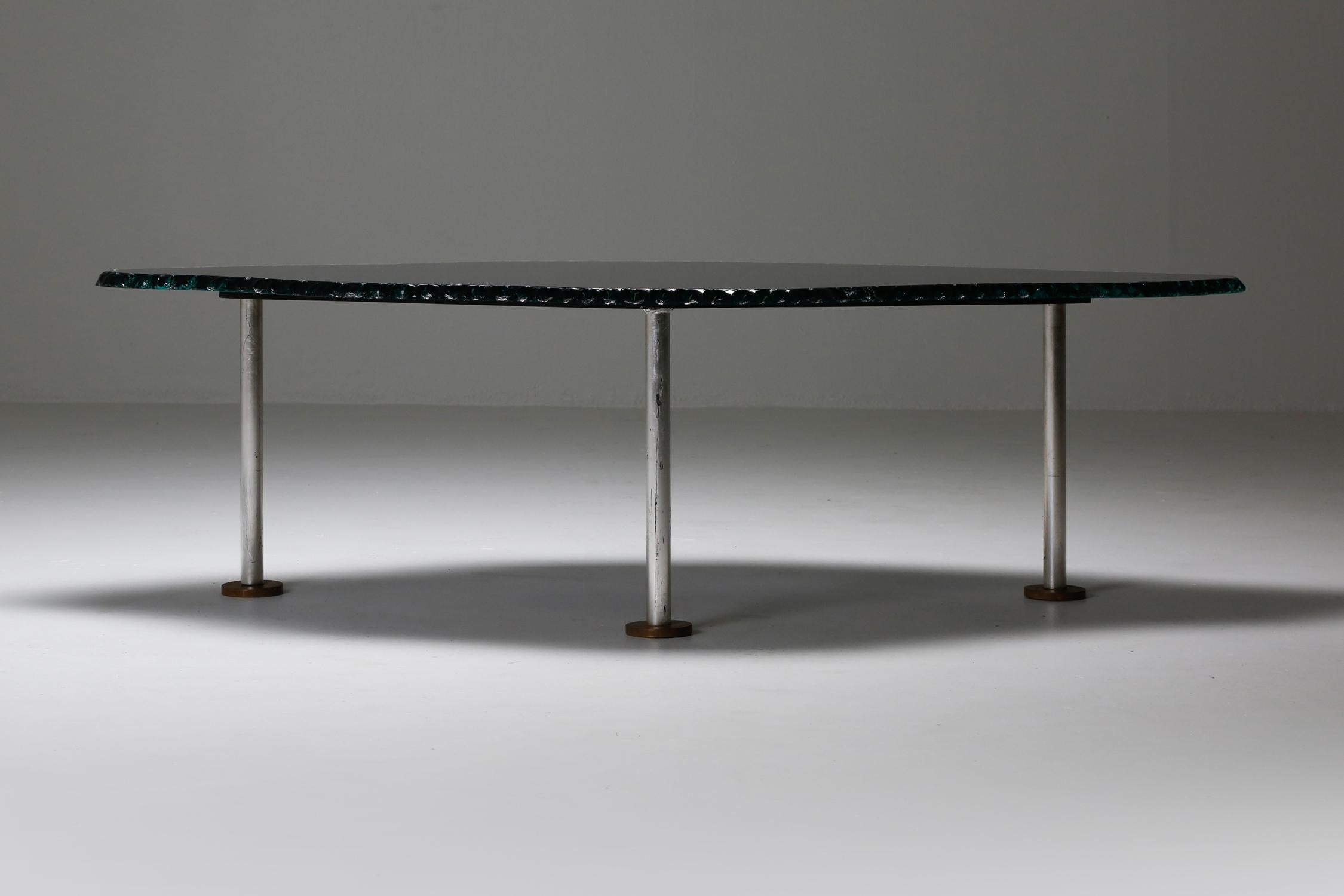 Table basse post-moderne italienne, un véritable chef-d'œuvre qui résume l'esprit de l'ère du design des années 1980. Dotée de trois pieds chromés élégants et d'un plateau en verre imparfait, cette table basse apporte une touche unique et