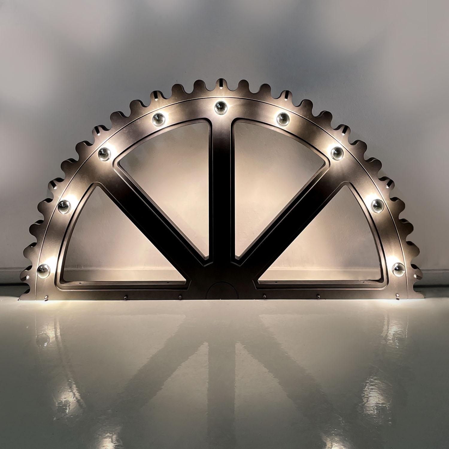 Italian post-modern illuminated glitter grey semicircle mechanism prop, 2020s
Illuminated semicircle prop made of mdf. This prop represents half of a mechanism or a wheel, and is lacquered dark gray with a glitter finish. There are nine light