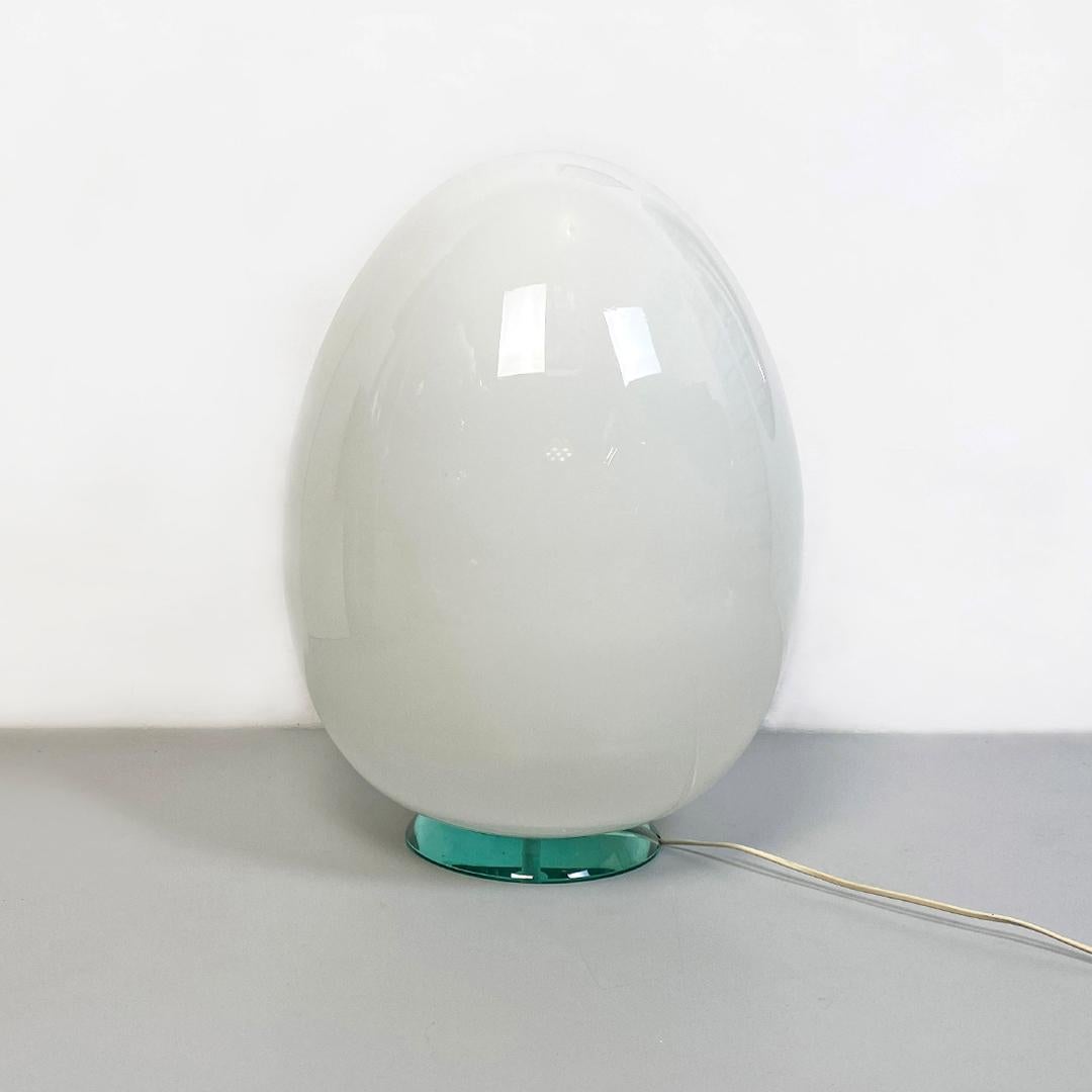Lámpara huevo italiana postmoderna de sobremesa o de pie, de vidrio con leche, con base aguamarina, años 80.
Lámpara de sobremesa o de pie con difusor en forma de huevo de cristal blanco leche, con carcasa sobre base redonda de cristal verde