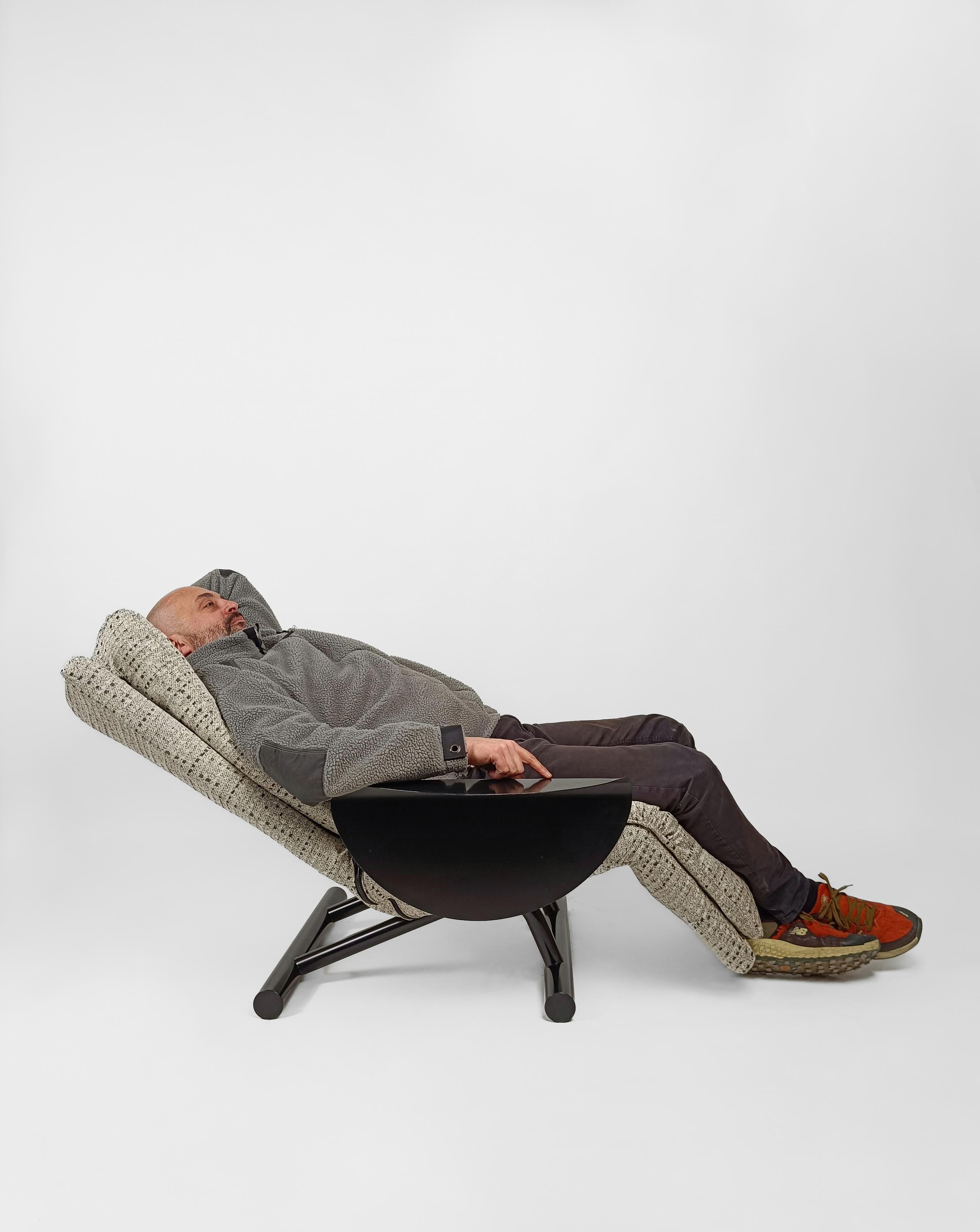 Une chaise de salon post-moderne qui se transforme en une seconde en
chaise longue.

Il suffit de lever l'accoudoir, un disque de métal noir plié avec le même naturel qu'un origami, de décider de l'inclinaison de la chaise longue et de l'abaisser