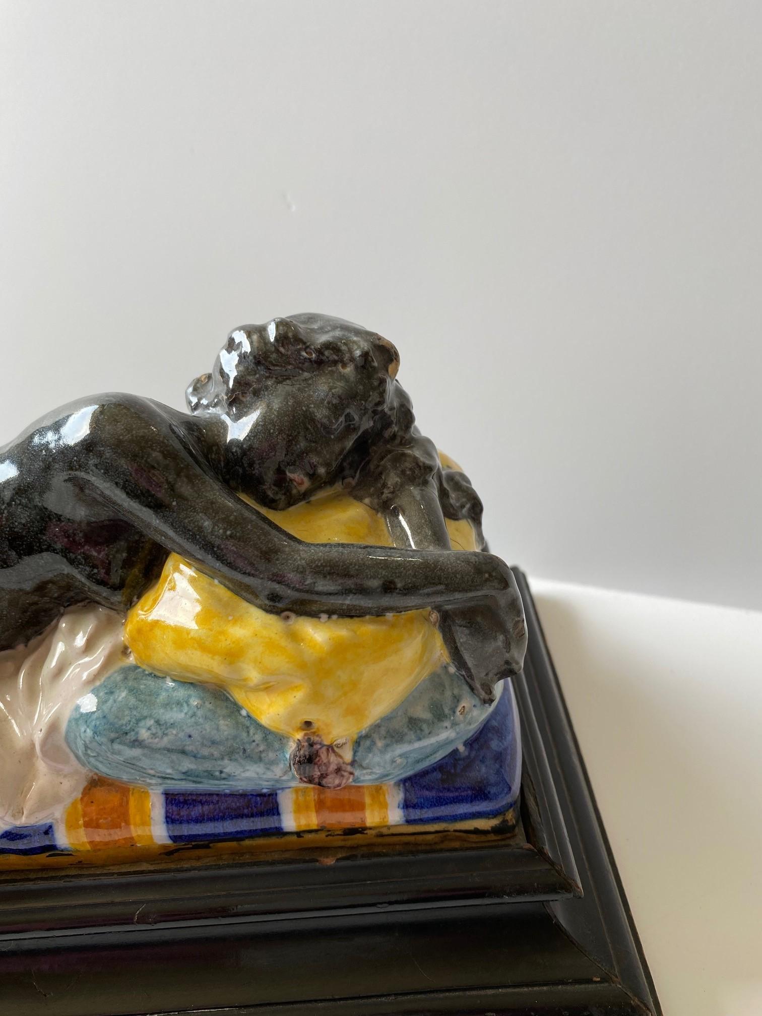 Una donna nuda sdraiata su una ceramica color malto con una base in legno ebanizzato.