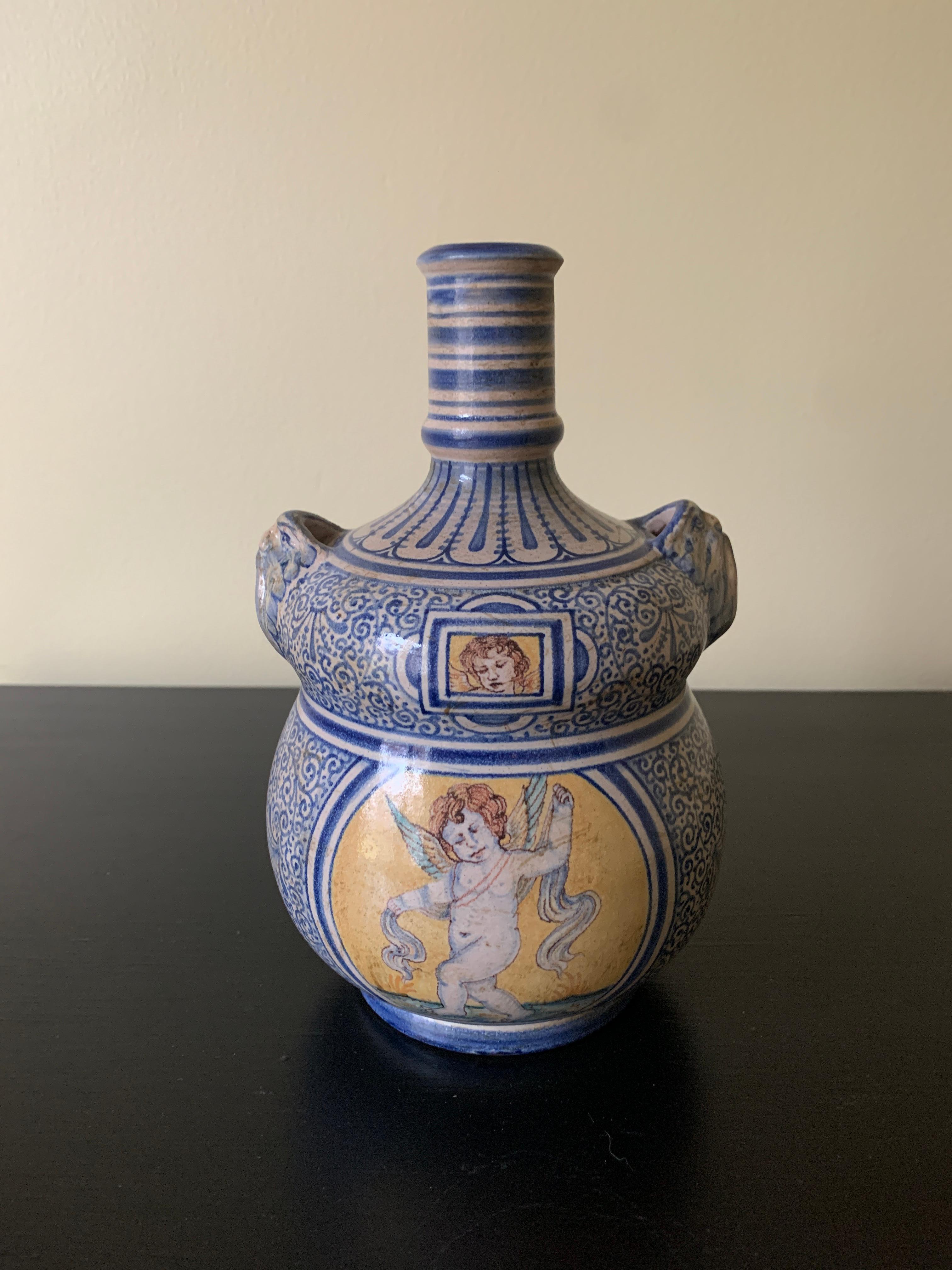 A beautiful hand painted blue, white, and yellow faience pottery jug or vase with handles featuring classical putti 

By Deruta

Italy, Late 20th Century

Measures: 5