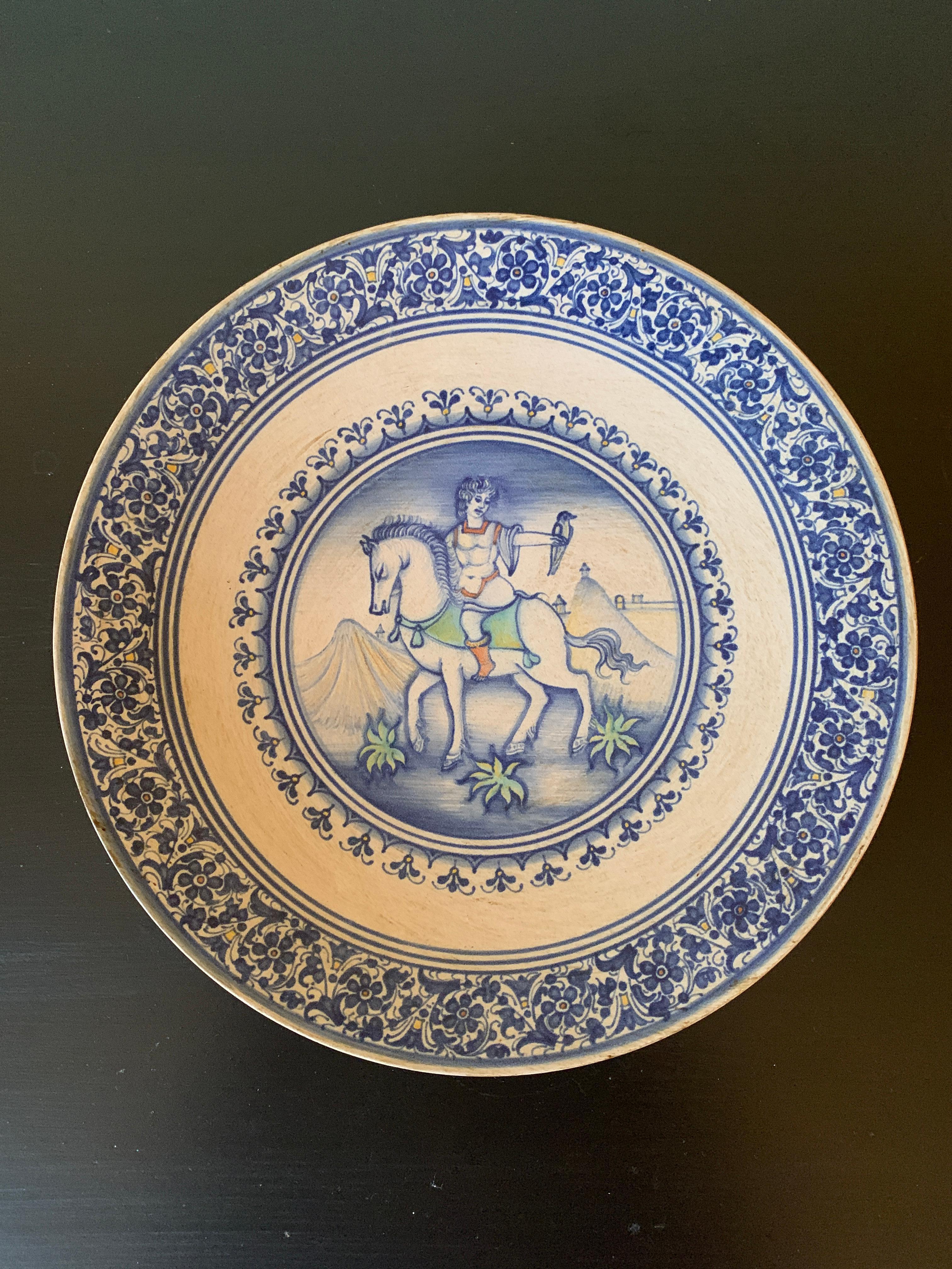 A beautiful hand painted blue, cream, and green faience pottery wall plate featuring an allegorical scene of a man riding a horse with a bird on his arm.

By Cynthia Deruta

Italy, Late-20th Century

Measures: 9.75