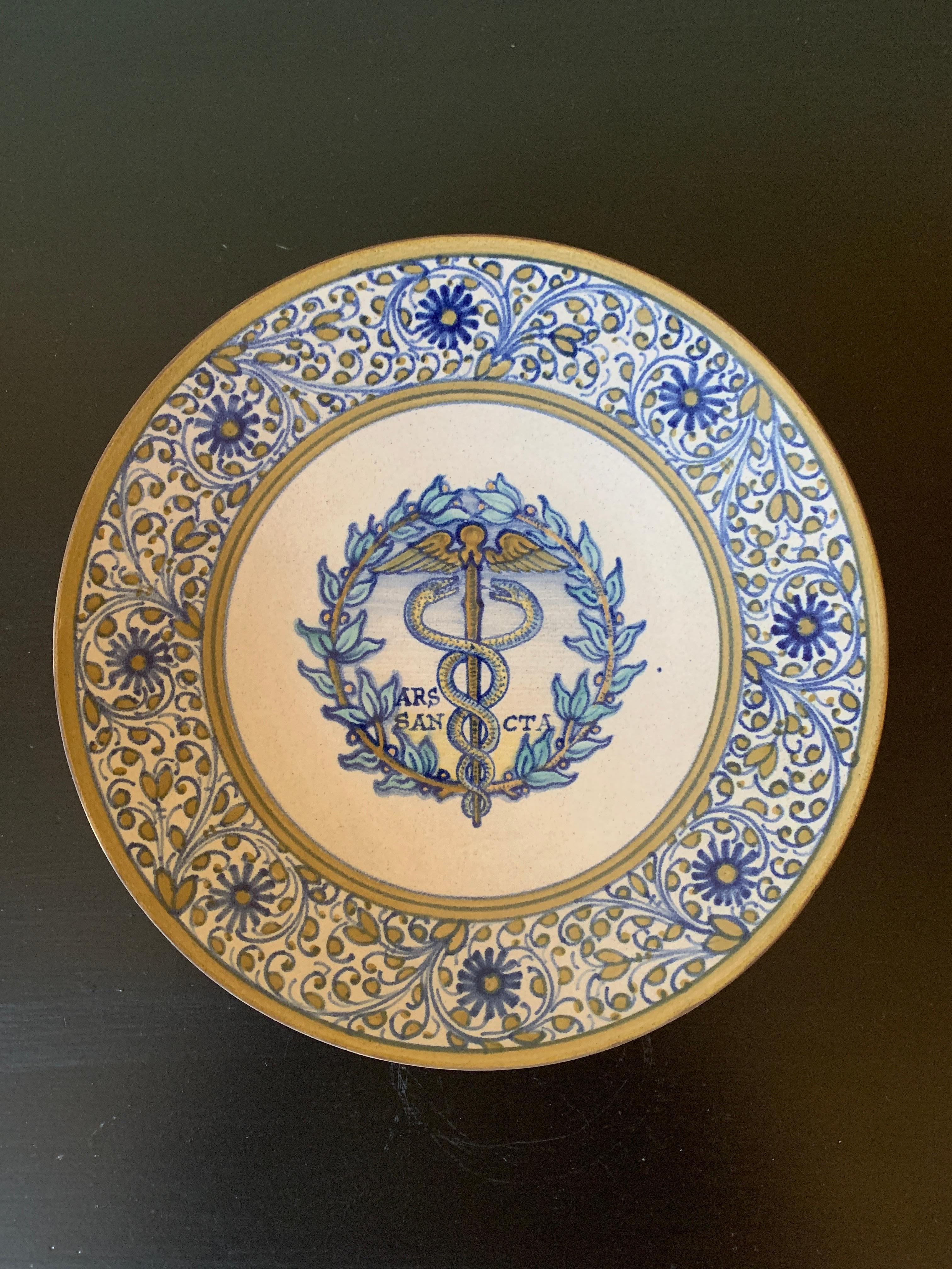 A beautiful hand painted blue, cream, and yellow faience pottery wall plate featuring the caduceus. The caduceus is the staff carried by Hermes in Greek mythology and consequently by Hermes Trismegistus in Greco-Egyptian mythology. The same staff