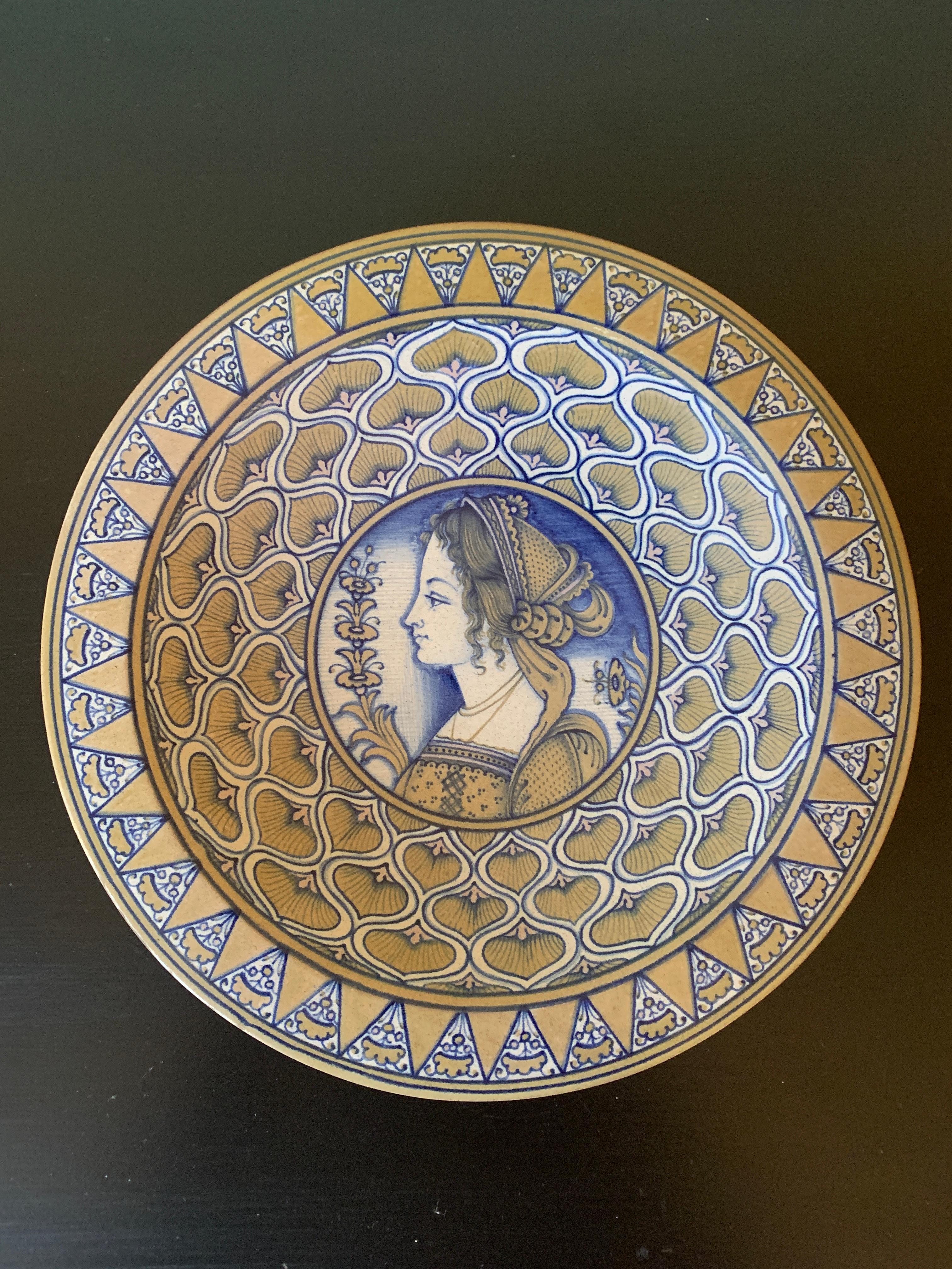 Un bellissimo piatto da parete in ceramica faience blu, crema e giallo dipinto a mano con un ritratto femminile e disegni geometrici.

Di Cynthia Deruta

Italia, fine del XX secolo

Misure: 10 