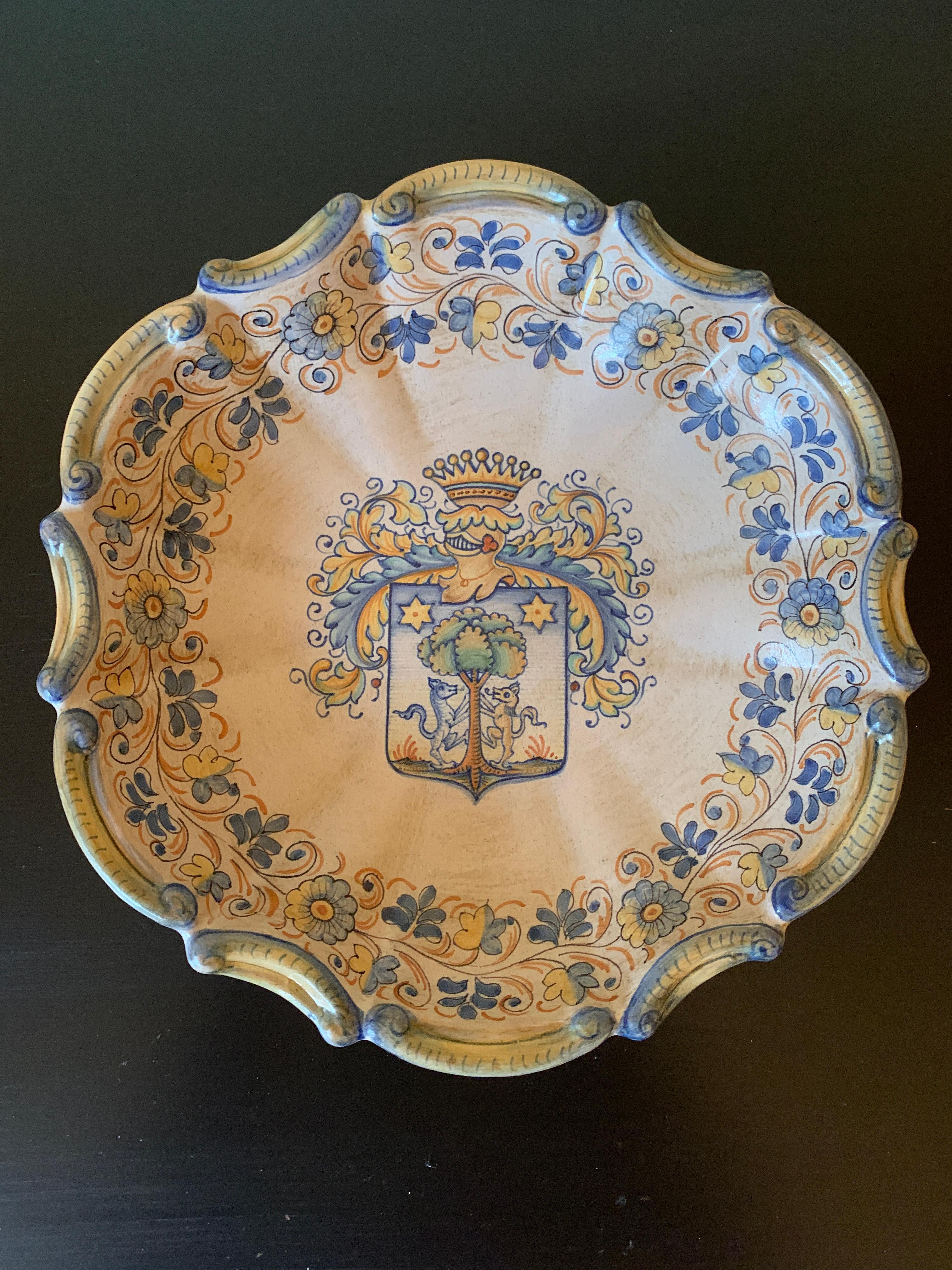A beautiful hand painted blue, cream, and yellow faience pottery wall plate featuring a coat of arms crest, and a floral scalloped border

By Cynthia Deruta

Italy, Late-20th Century

Measures: 10