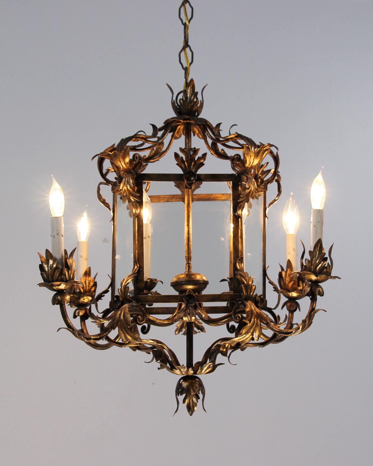 Beautiful, 1950s Italian gilt iron chandelier in the Provincial style. The chandelier features 6 arms flowing gracefully from a glass paneled lantern-shaped center. The chandelier’s design and scale would make it a wonderful addition wherever it may