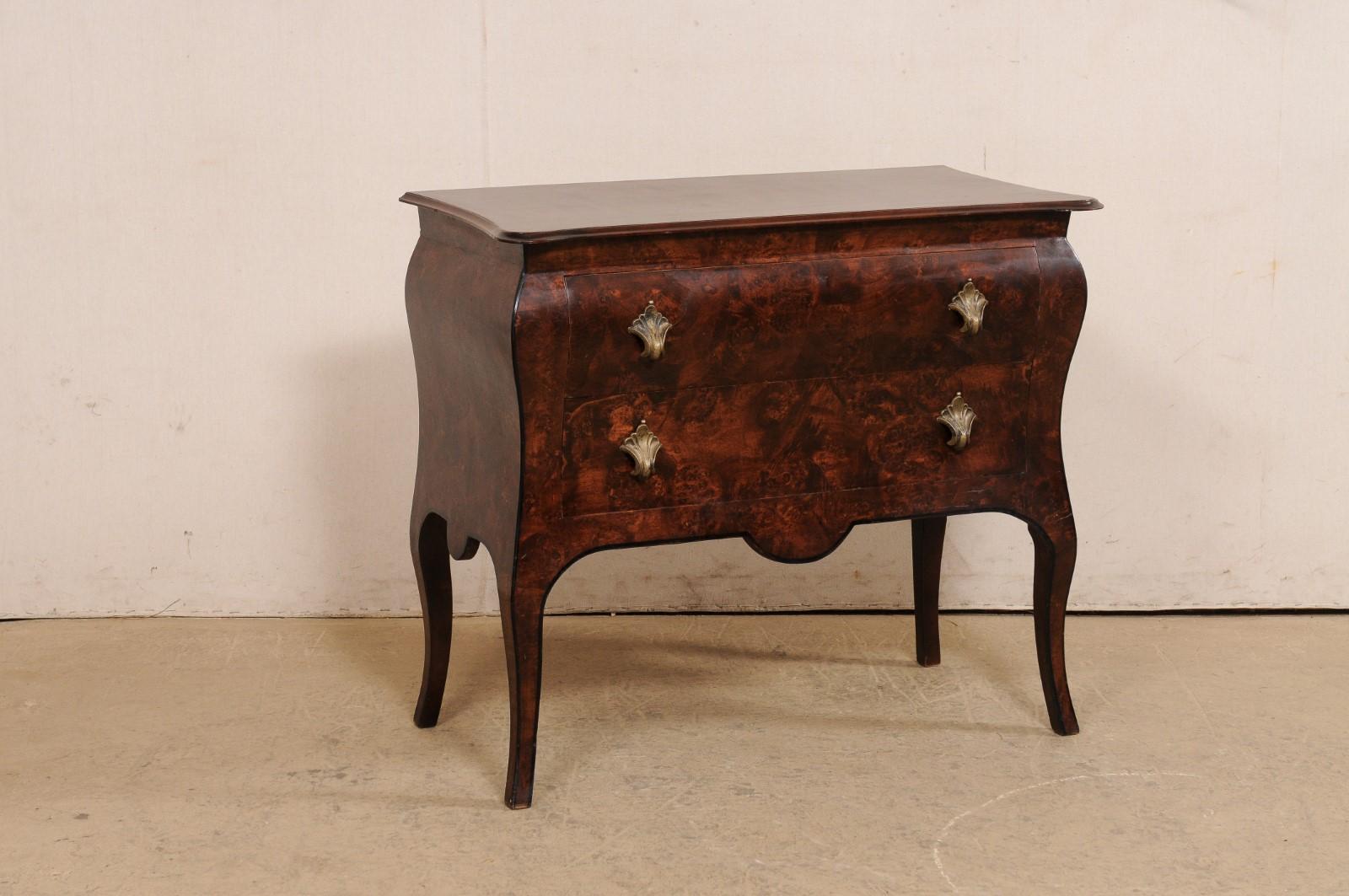 An Italian raised chest of two drawers with burled wood veneer. This vintage chest from Italy is abundant with softly curved lines; a top with rounded front corners and a shallow convex front, a slightly bowed body, single scallops adorning the