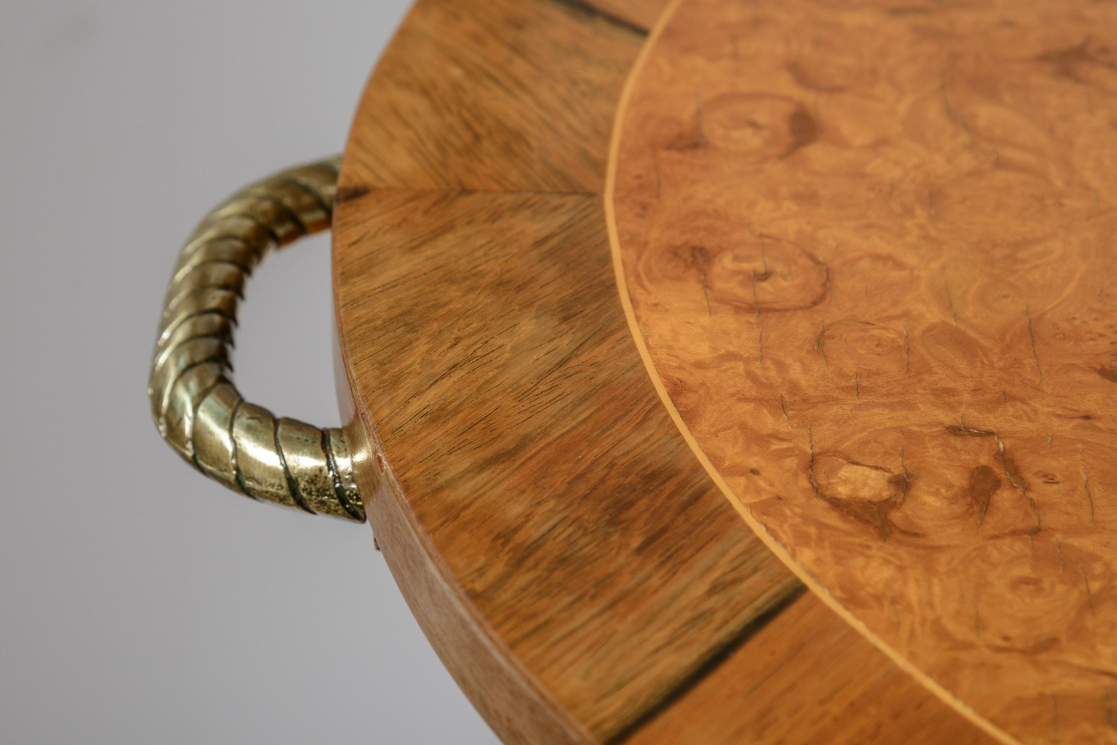 This is a striking  Burl Veneer and Brass three tier table with brass handles that  stands on brass casters.
It  is oval in shape, four Brass mounts ending in casters and finished at the top with brass finials.
This table is also a Trolley or could