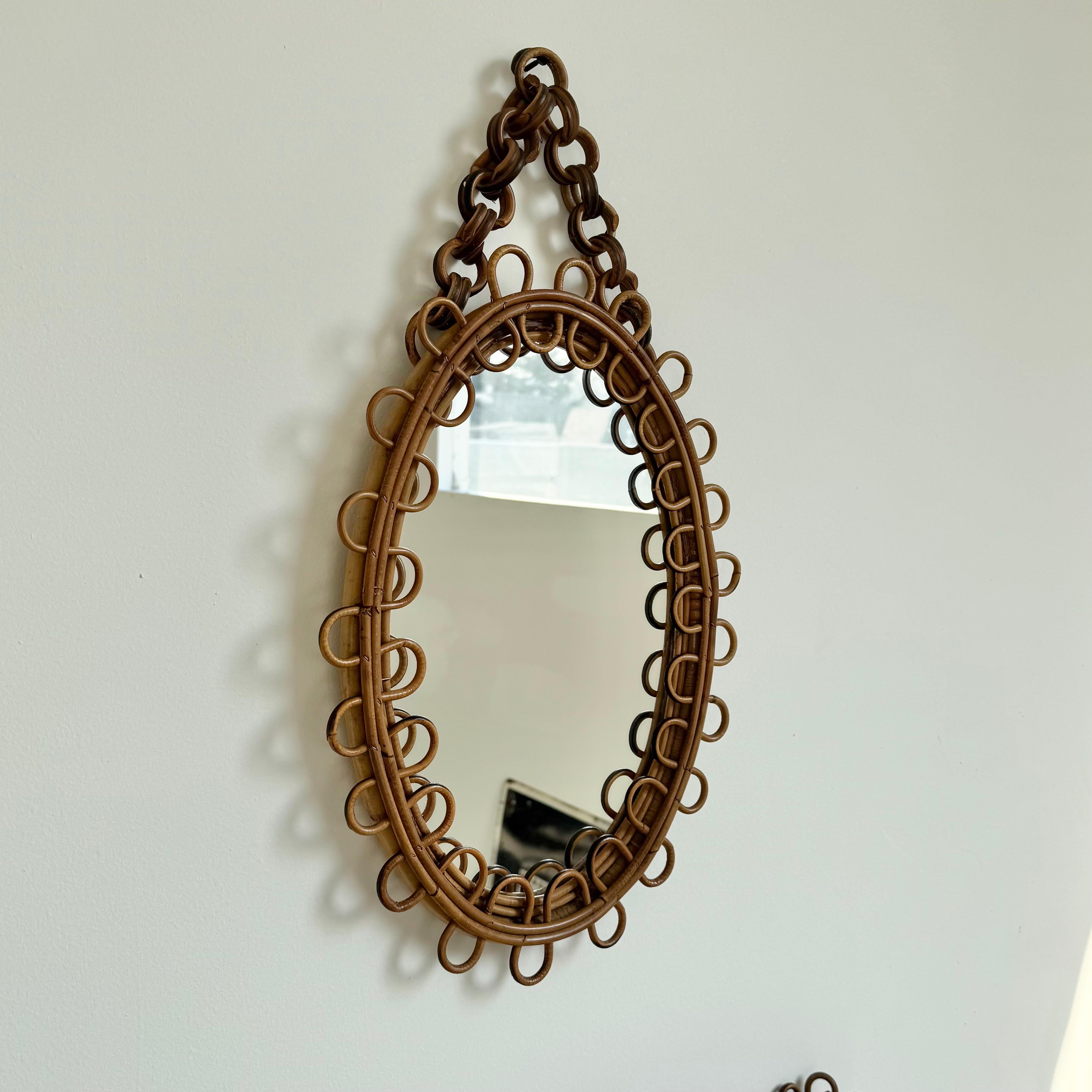 Elegant rattan mirror with matching table, made in Italy, circa 1950s. Undulating rattan adorns the mirror and table edges. Ovular mirror with rattan link strap for hanging. Mirror is just under 23