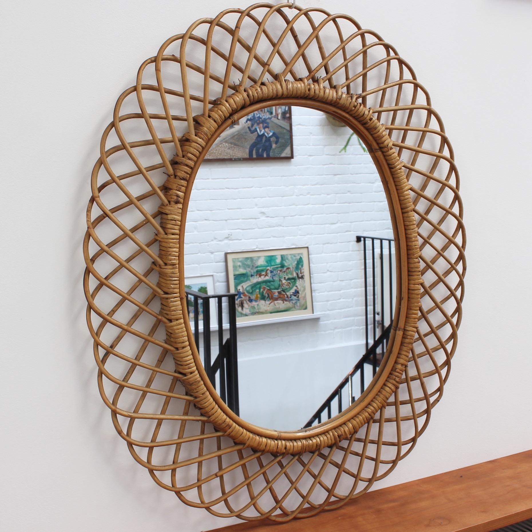 Italian rattan wall mirror (circa 1960s) in the style of Franco Albini. This mirror has a complex weave of rattan in a series of horseshoe-shaped projections on the frame edge. There is a graceful, aged patina on the mirror frame and the rattan