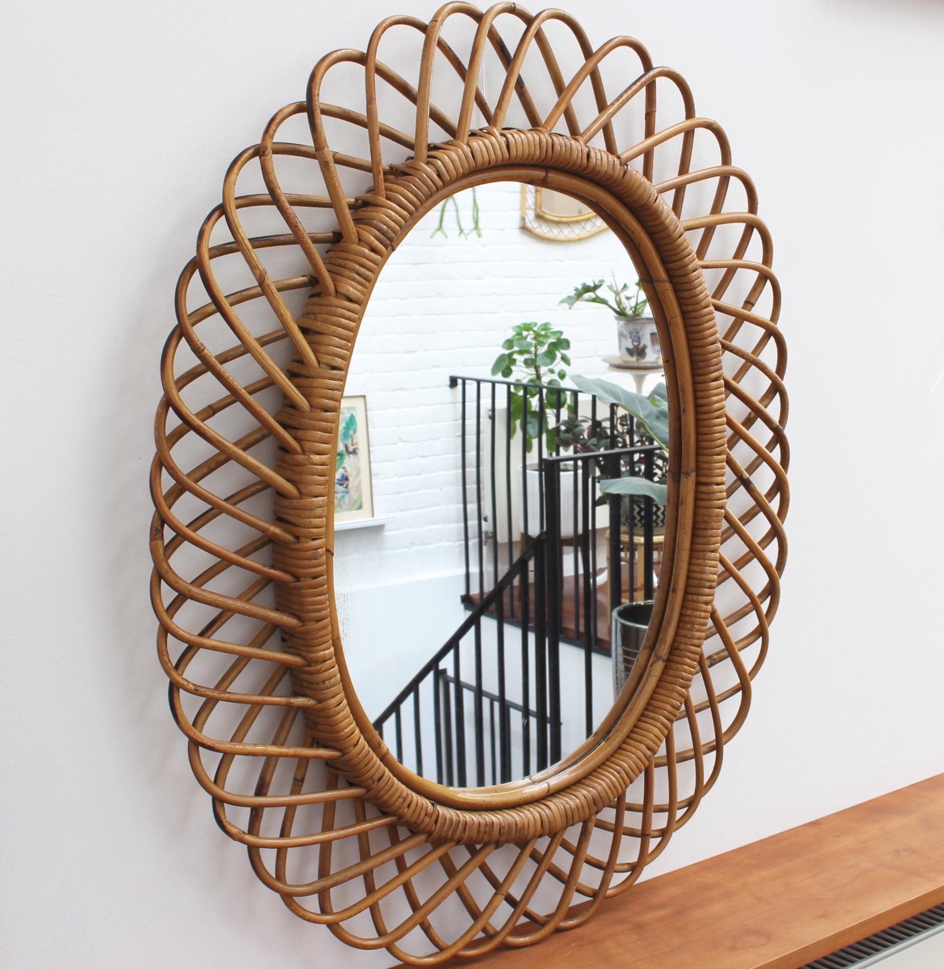 Italian rattan wall mirror, circa 1960s in the style of Franco Albini. This mirror has a complex weave of rattan in a series of horseshoe-shaped projections on the frame edge. There is a graceful, aged patina on the mirror frame and some blemishes