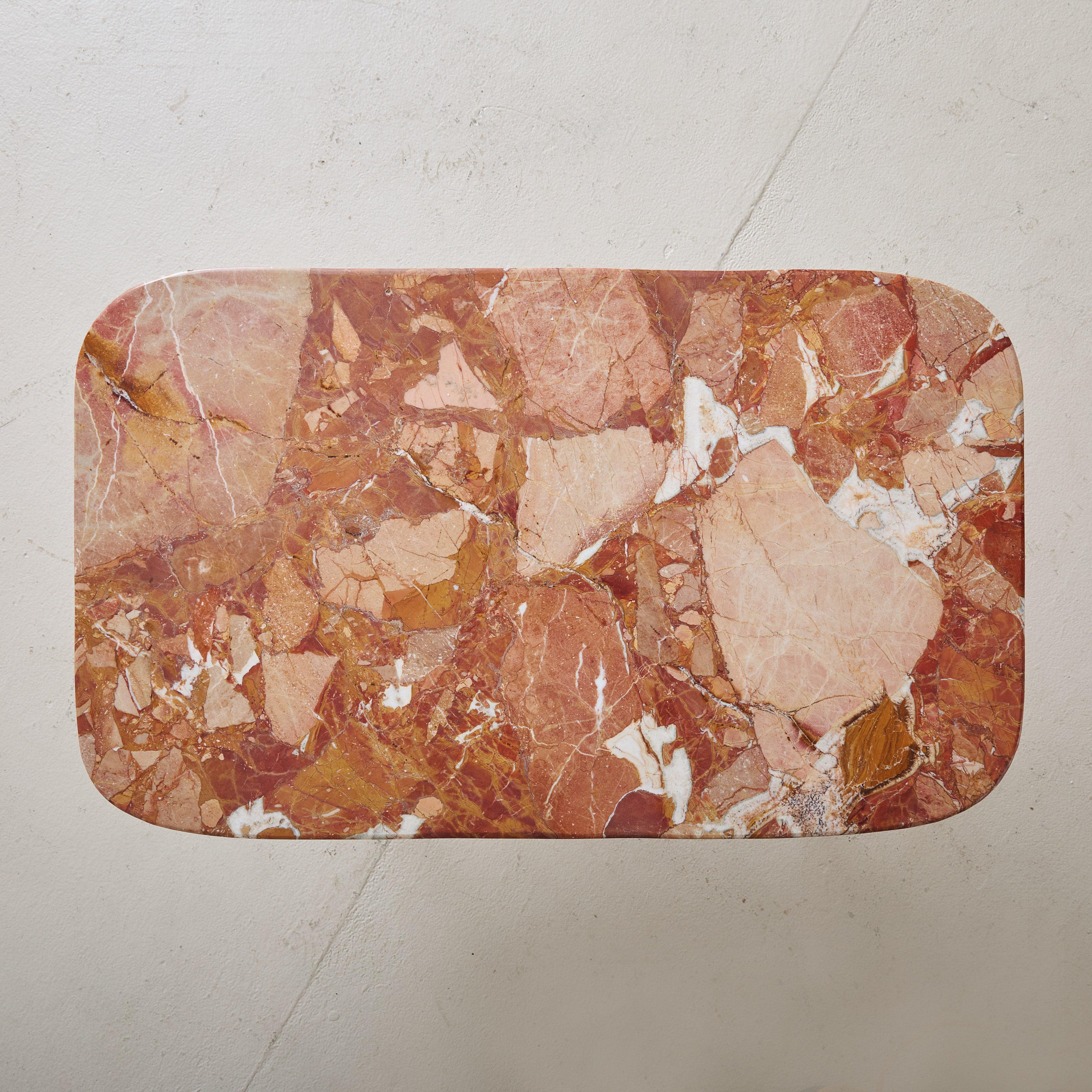 A 1950s Italian coffee table featuring a rectangular Breccia Pernice marble tabletop with subtly rounded corners. The marble has striking veining in a range of brick red, blush, and tangerine hues. This table stands on angled, tapered black metal