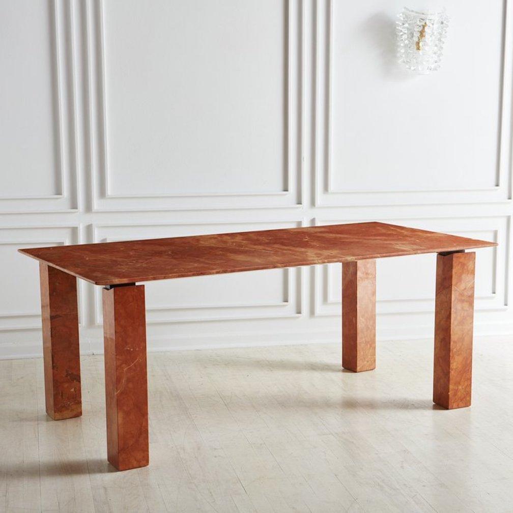 A stunning Red Verona marble dining table in a polished laminate finish. This rectangular table has four square legs that angle at the top. This table has a steel frame that attaches to the legs and supports the tabletop, making it appear to