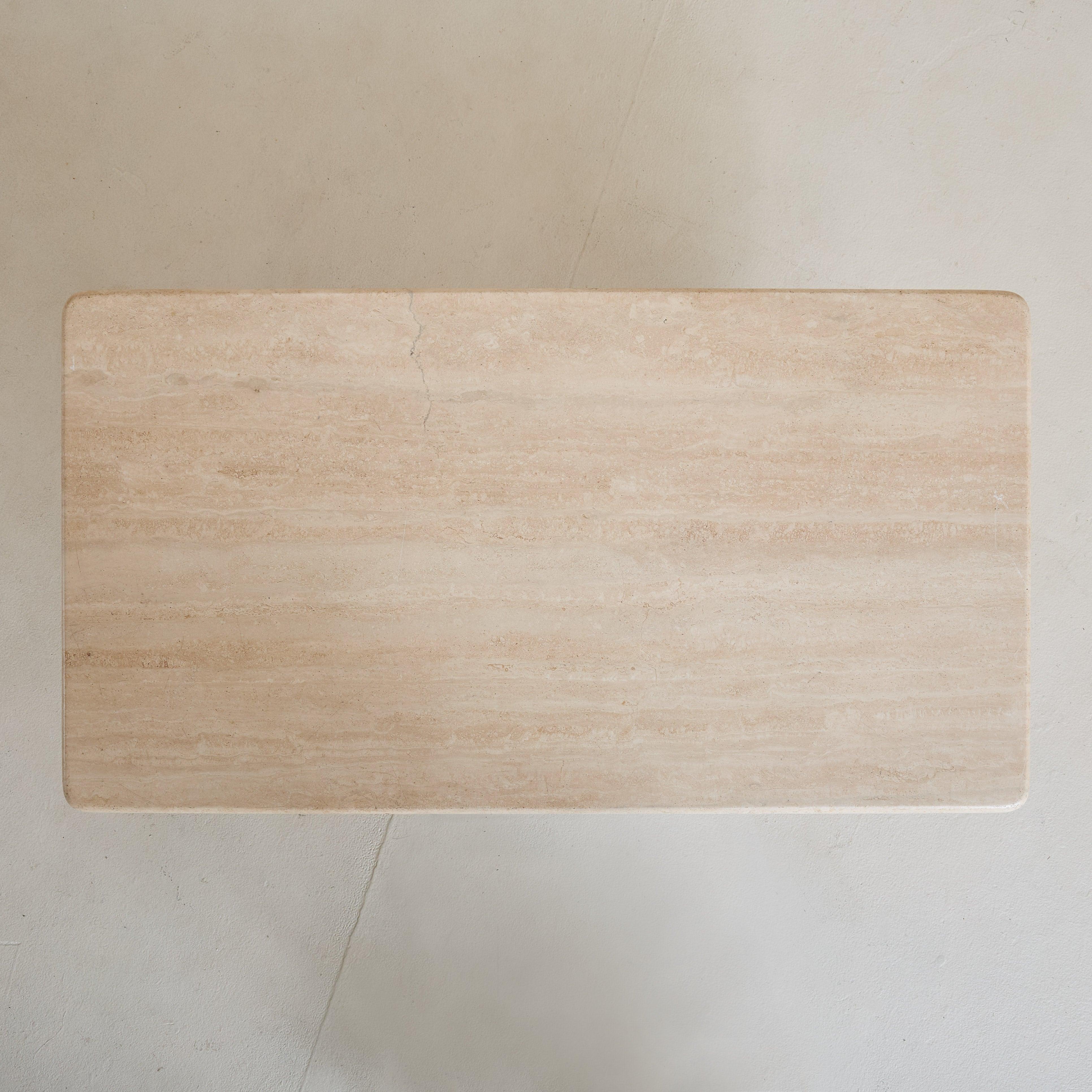 A 1970s Italian coffee table defined by a rectangular travertine top, featuring subtle, fluid veining in ivory and beige hues. The generously proportioned natural stone is supported by a geometric black iron base. This piece strikes a perfect