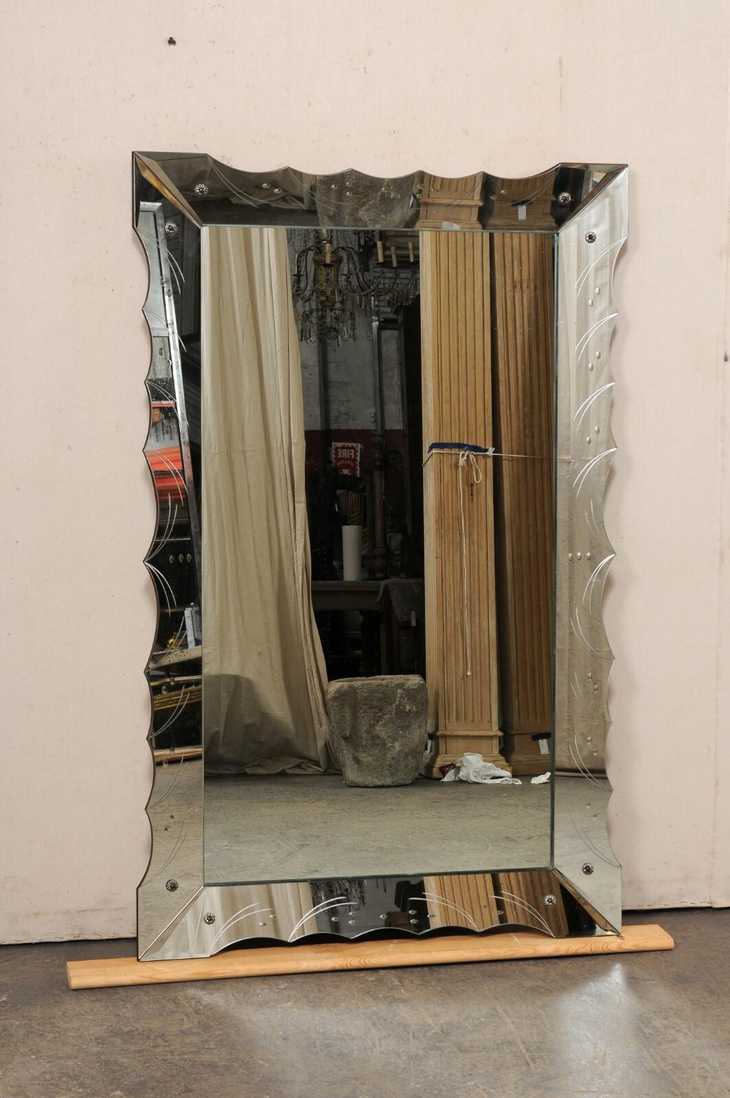 A large-sized Italian wall mirror with scalloped mirror frame. This vintage mirror from Italy features a rectangular-shaped clear mirrored glass center, which is recessed within a mirrored surround with scalloped perimeter and etched pattern and