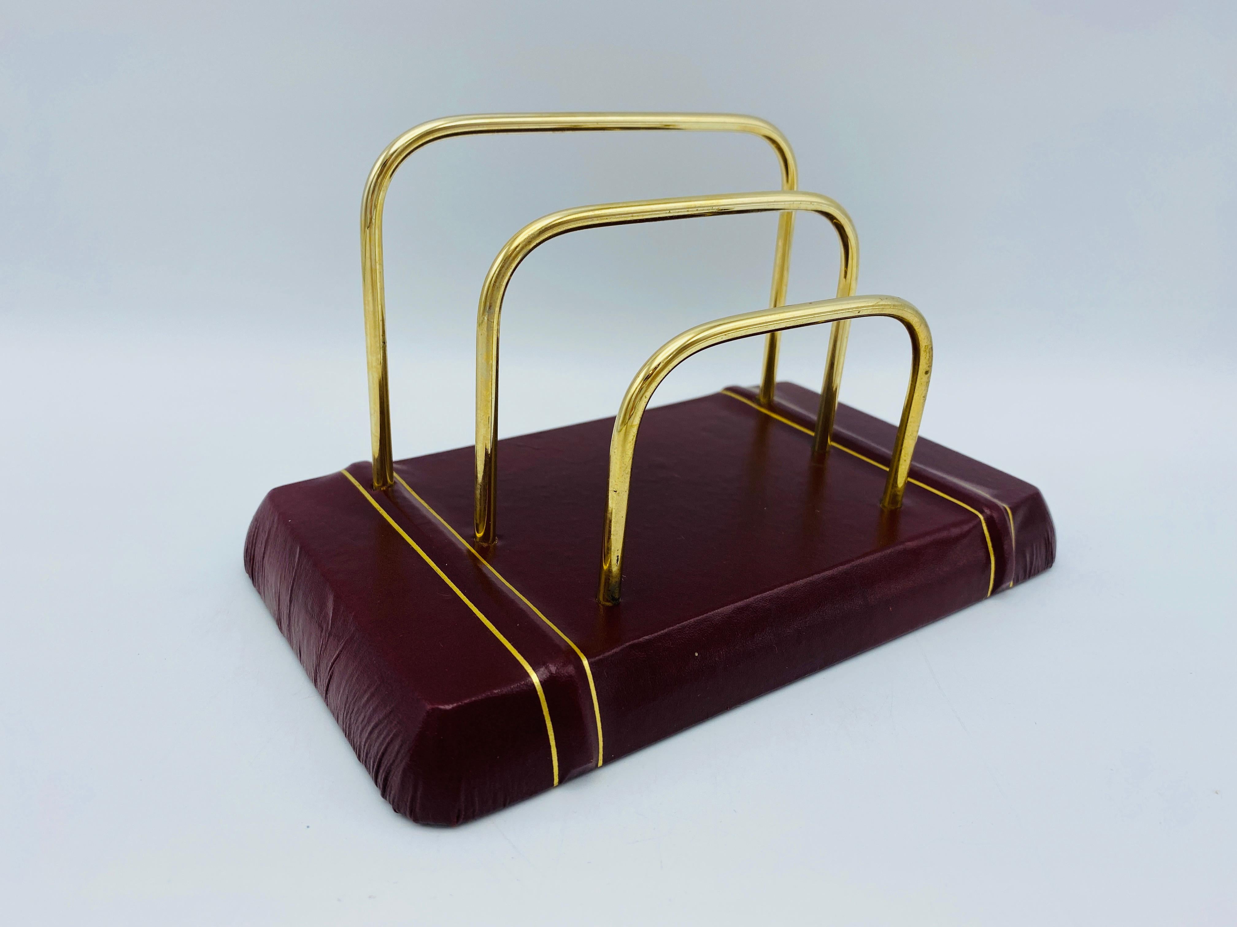 Listed is a gorgeous, Italian leather letter organizer, circa 1980s. The piece is covered in a deep burgundy red leather with gold debossed stripes (front to back). It has three brass arms to hold letters and other papers upright. Felt underside.