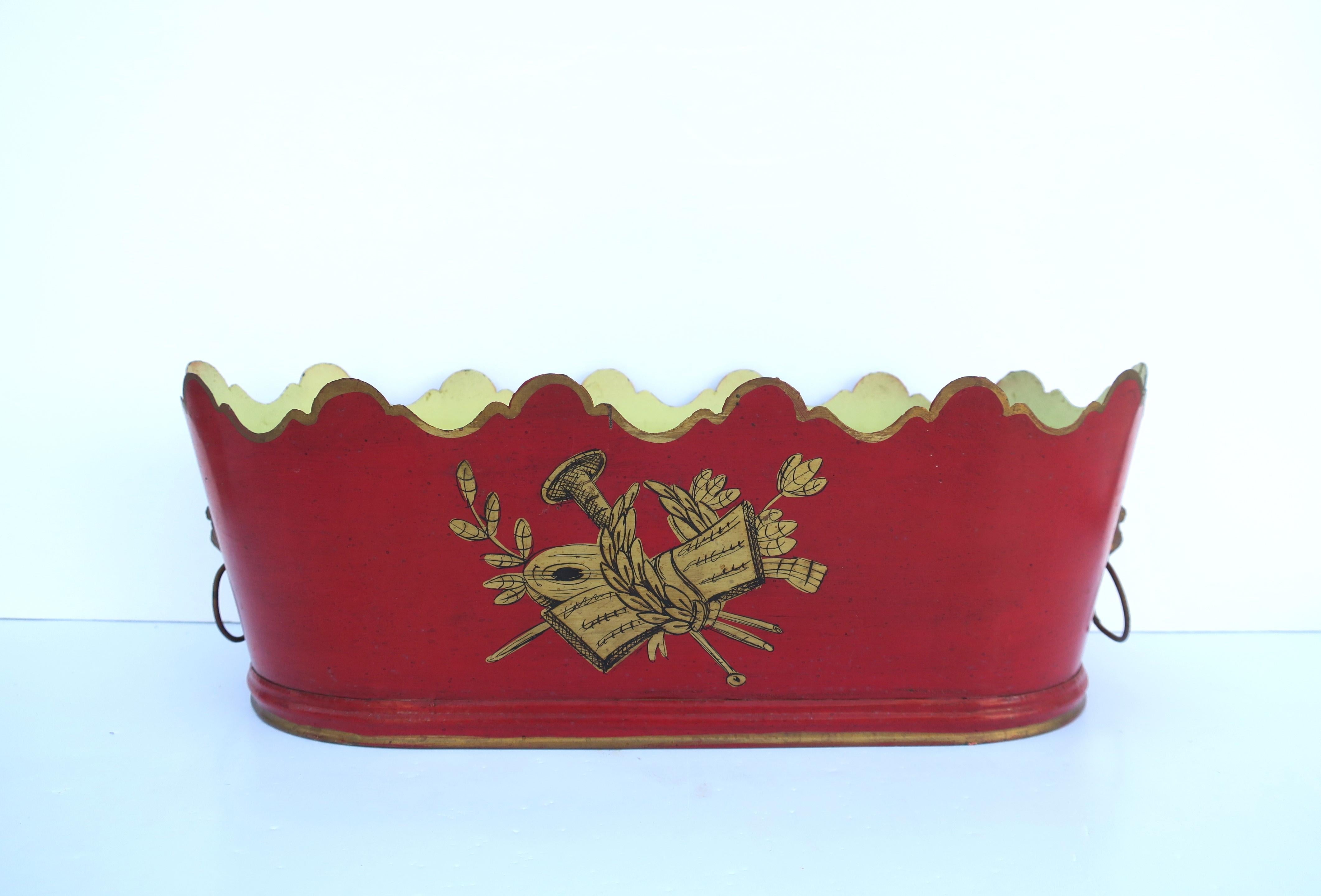 A beautiful Italian red and gold metal tole plant or flower planter cachepot jardiniere with lion head design, in the Regency style, circa mid to late 20th century, Italy. Piece is red metal tole with scalloped edge design in gold, gold design at