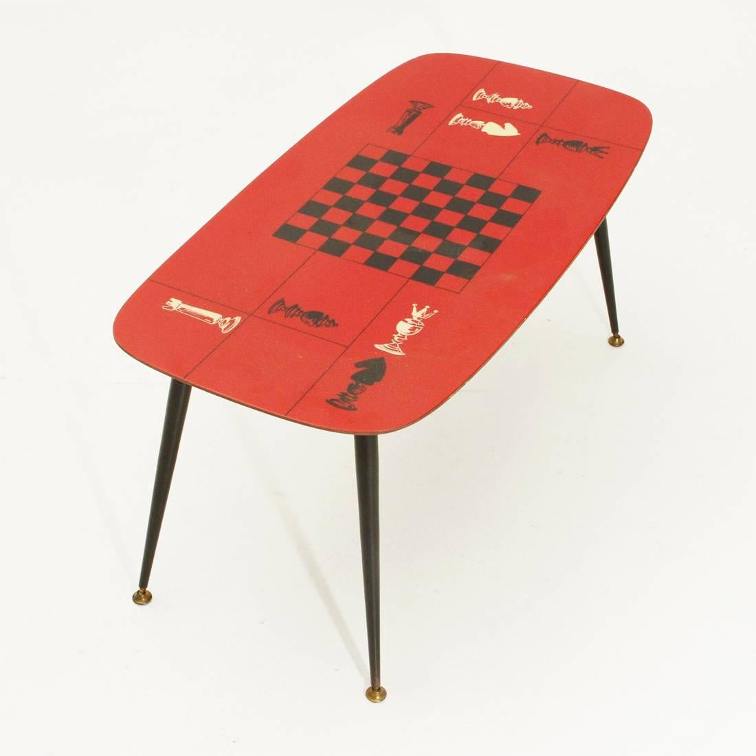 Italian manufacturing table produced in the 1950s.
Wooden top with red laminate surface.
Decorations depicting the game of chess.
Legs in black painted metal with adjustable brass feet.
Good general conditions, some signs due to normal use over