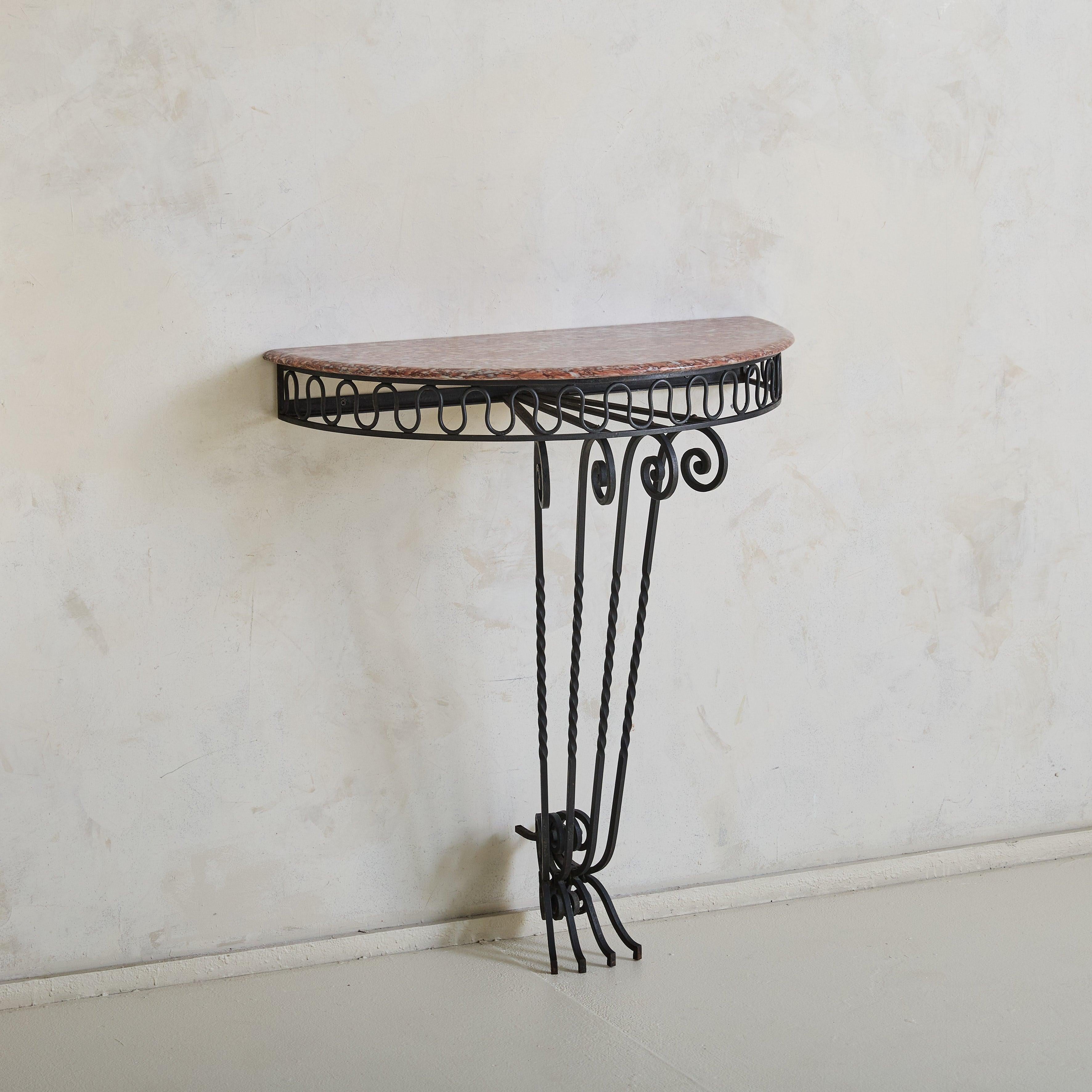 A 1950s Italian wall-mounted console, defined by its richly veined red marble demilune top with accents of creamy white and bordeaux. The patinated iron frame features delicate scrollwork, squiggle motifs, and four twisted legs that converge at the