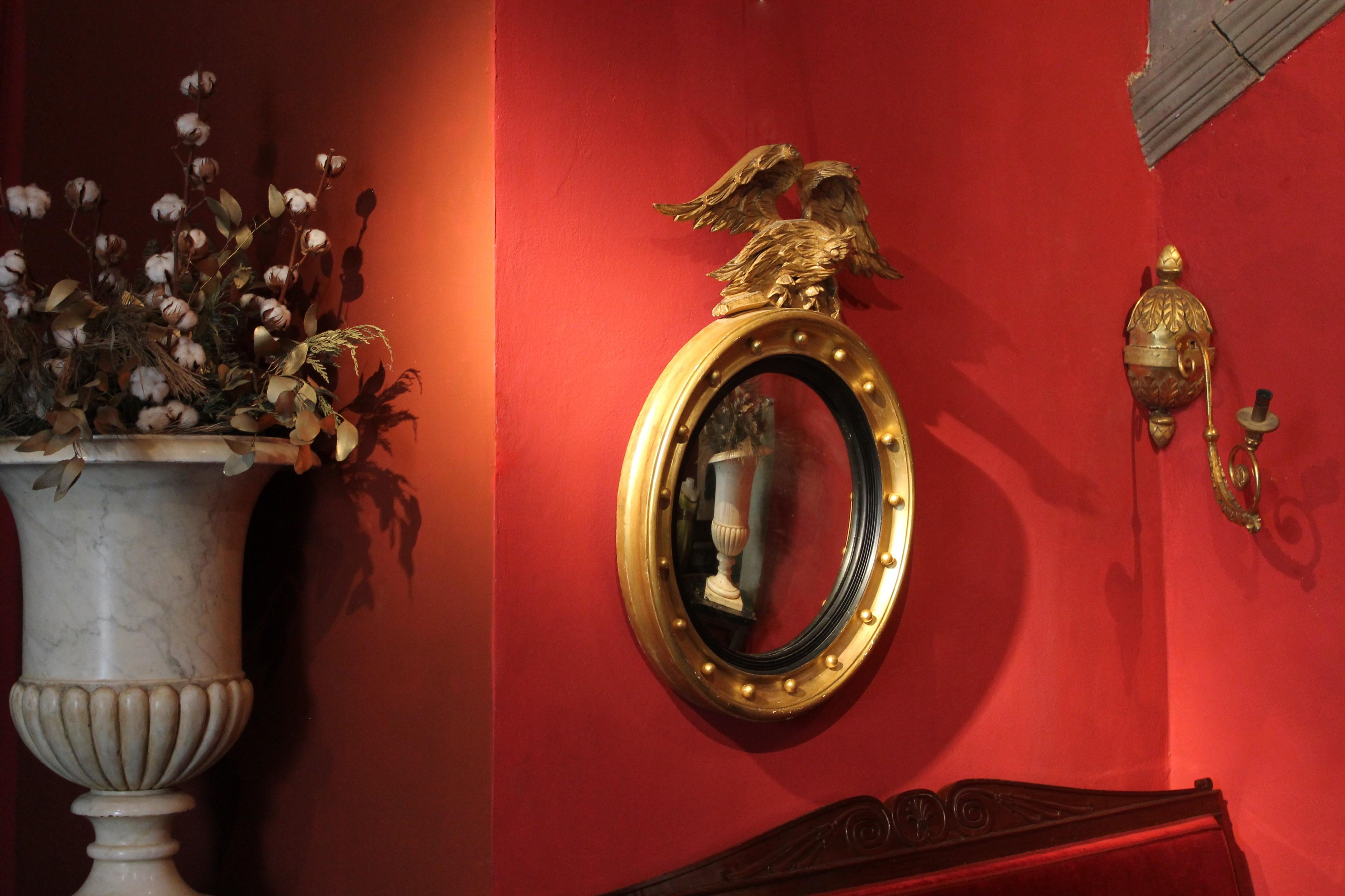 Dieser italienische, antike, konvexe Wandspiegel aus dem frühen 19. Jahrhundert mit der originalen Quecksilberspiegelplatte in einem Rahmen aus vergoldetem und ebonisiertem Holz, der von einem handgeschnitzten Adlergiebel aus vergoldetem Holz