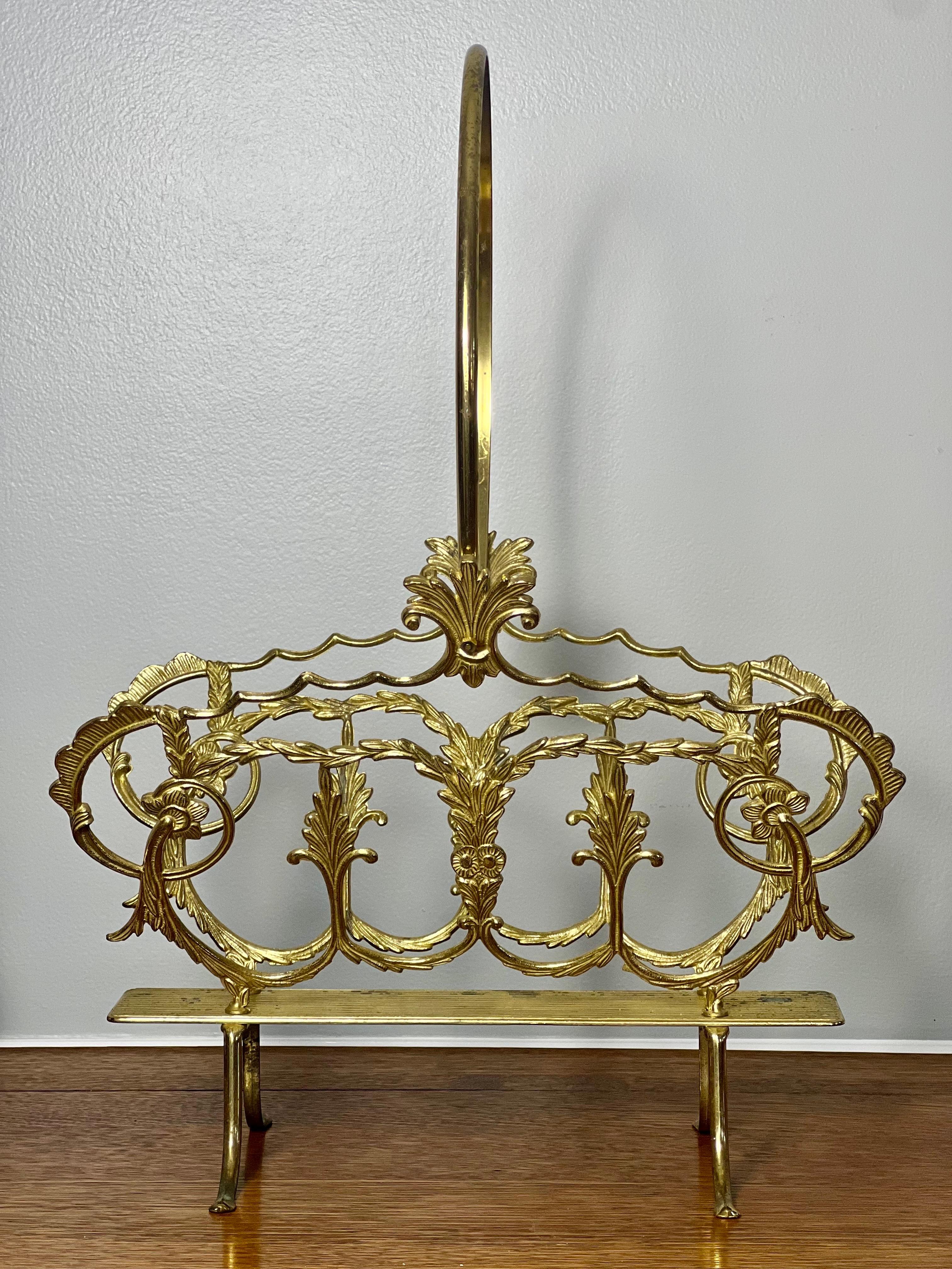 Vintage mid 20th century Italian Hollywood Regency brass magazine, book or log holder. This ornate footed brass basket features scrolling acanthus leaves and flowers with a large handle. Flowing lines and elements of nature lend a nod to Art