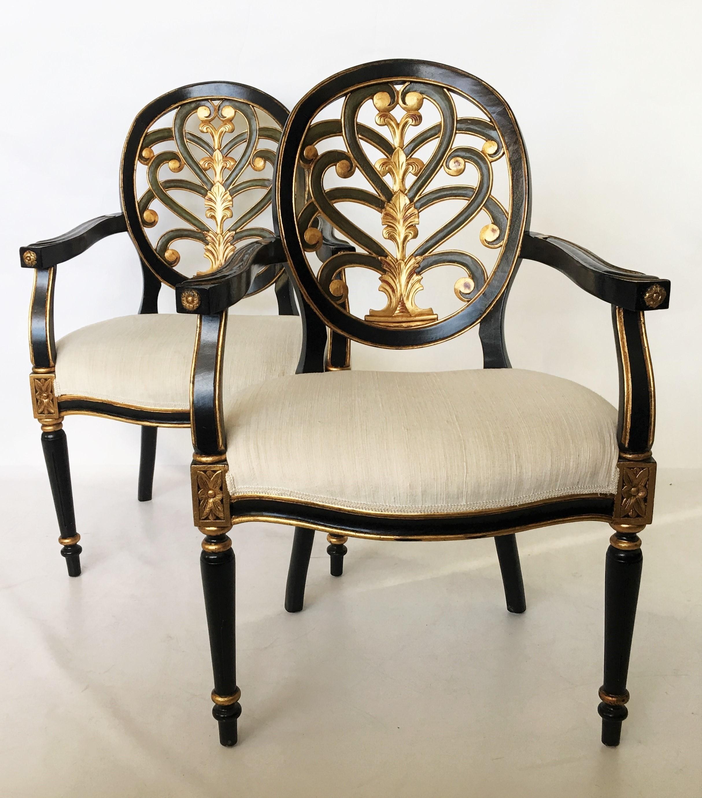 Superb pair of early 20th century Regency style armchairs in the neoclassical design. Ebonized chairs with an open carved oval back-splat with green and gold leaf accents. The seats are upholstered in a cream colored fabric at present but this could