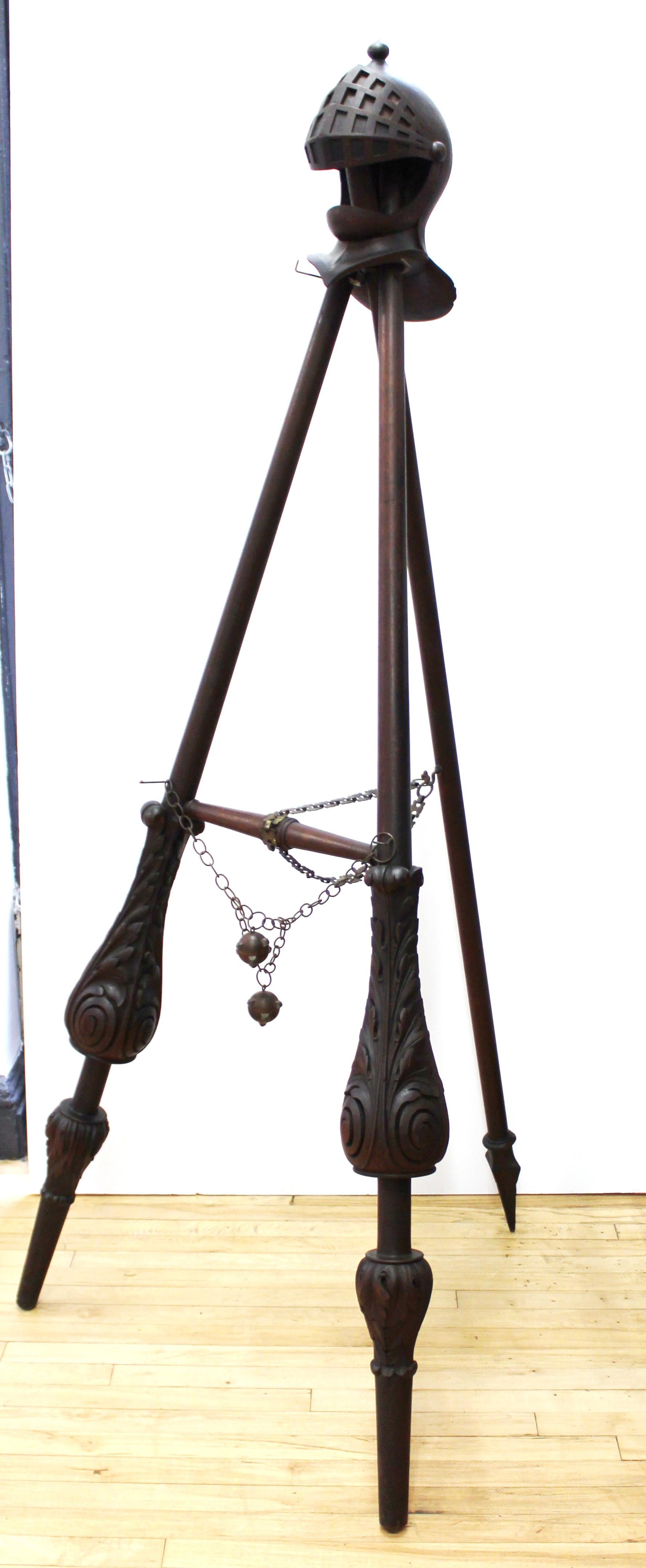 Italian Renaissance Revival monumental easel in hand carved mahogany wood, with jousting lances forming the legs and a large knight helmet finial. The two frontal jousting lance legs have elaborately carved ornamental acanthus leave foliage.