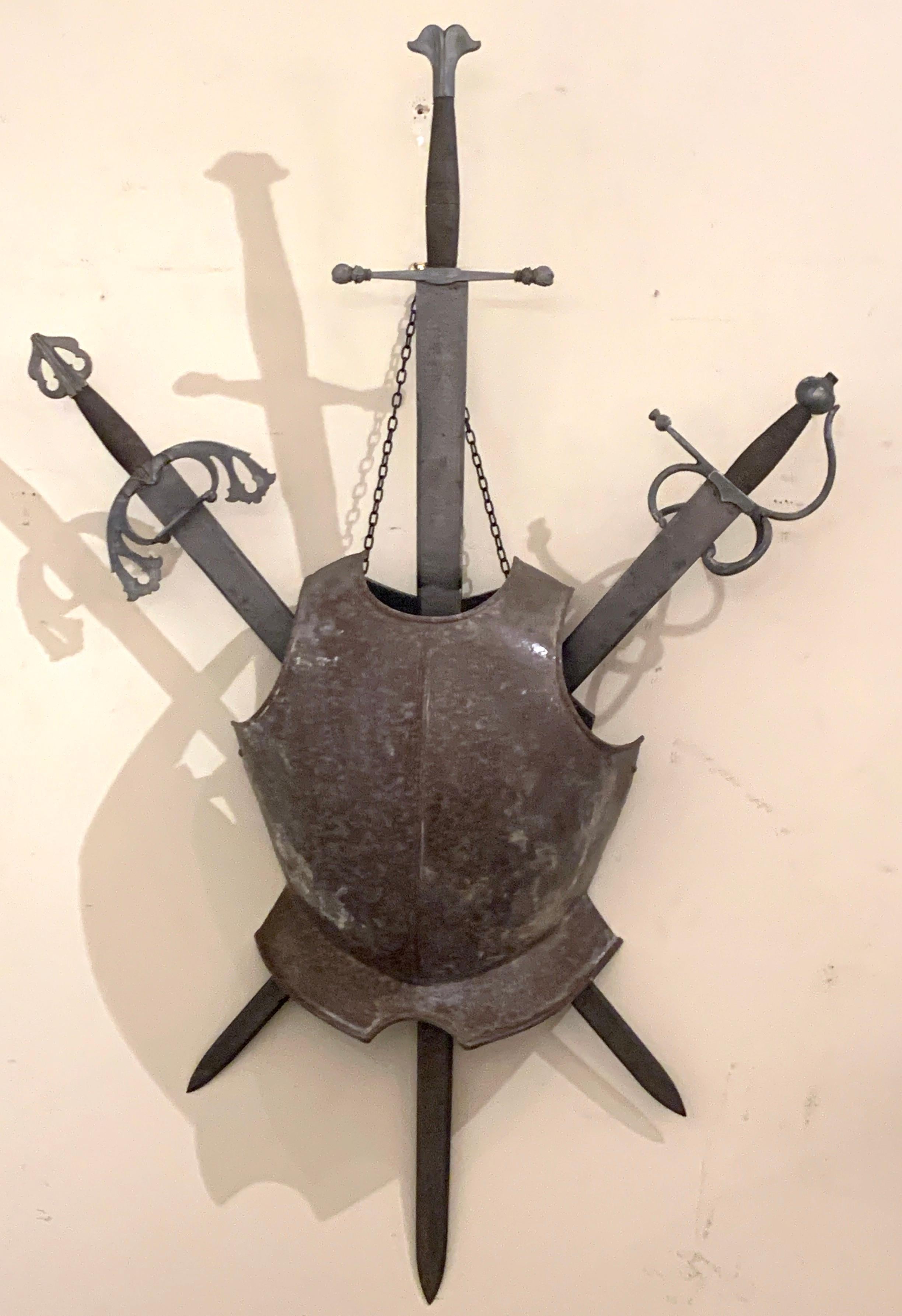 Italian Renaissance style arms and armour wall plaque, consisting of three forged steel and iron swords, with breast plate in front. Hanging on a chain linked wood back.