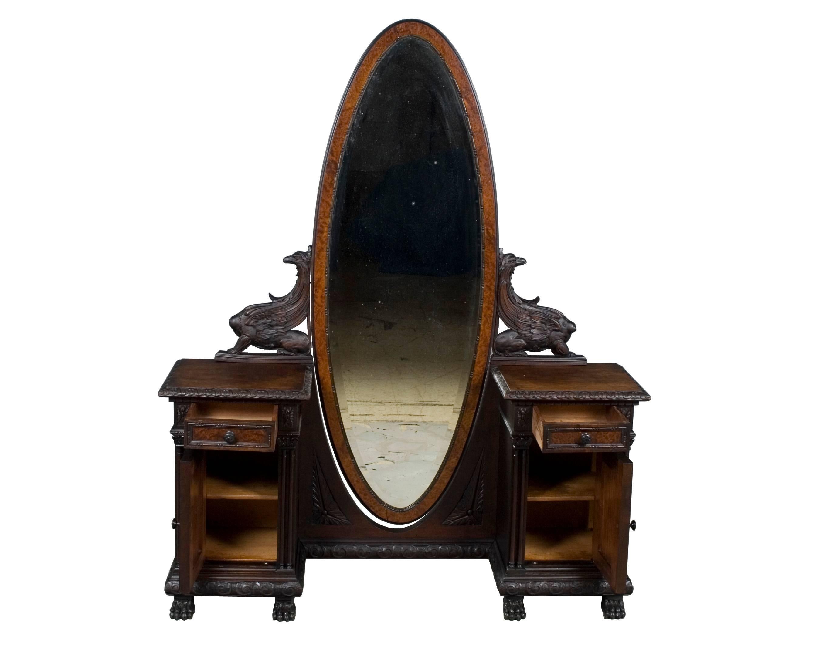 This beautiful carved walnut vanity was made circa 1940 in the Italian Renaissance style. It features a huge oval mirror with beveled glass flanked by carved griffon supports. These rest on two pedestals each with a drawer and cabinet. Inside each