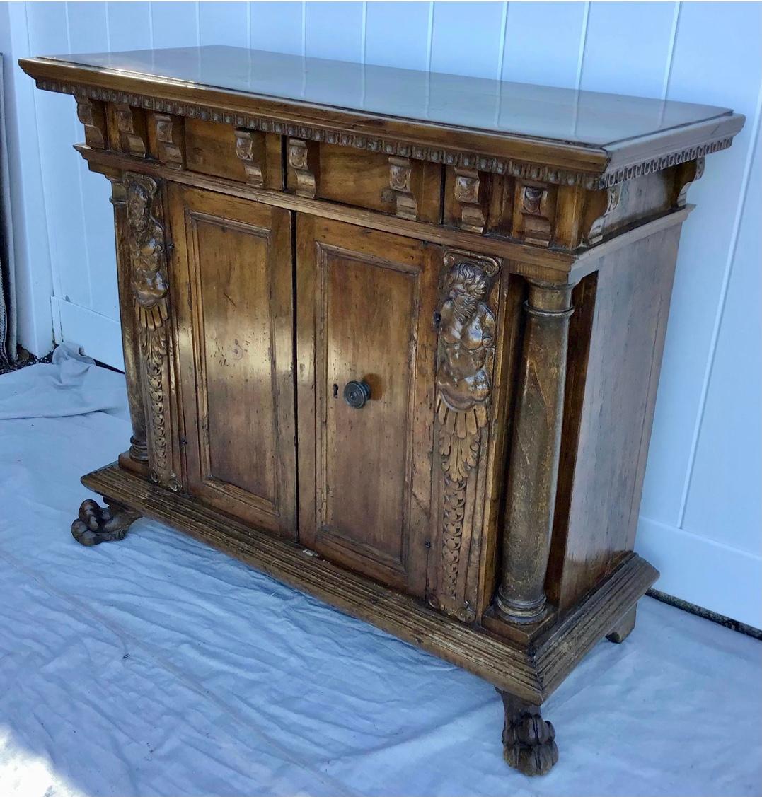 19th Century Italian walnut credenza. With old finish. Rectangular top with molded edge over a frieze with mounted corbels and two drawers over a pair of cabinet doors with original handle flanked by carved satyr, ending on lions paw feet. Solid and