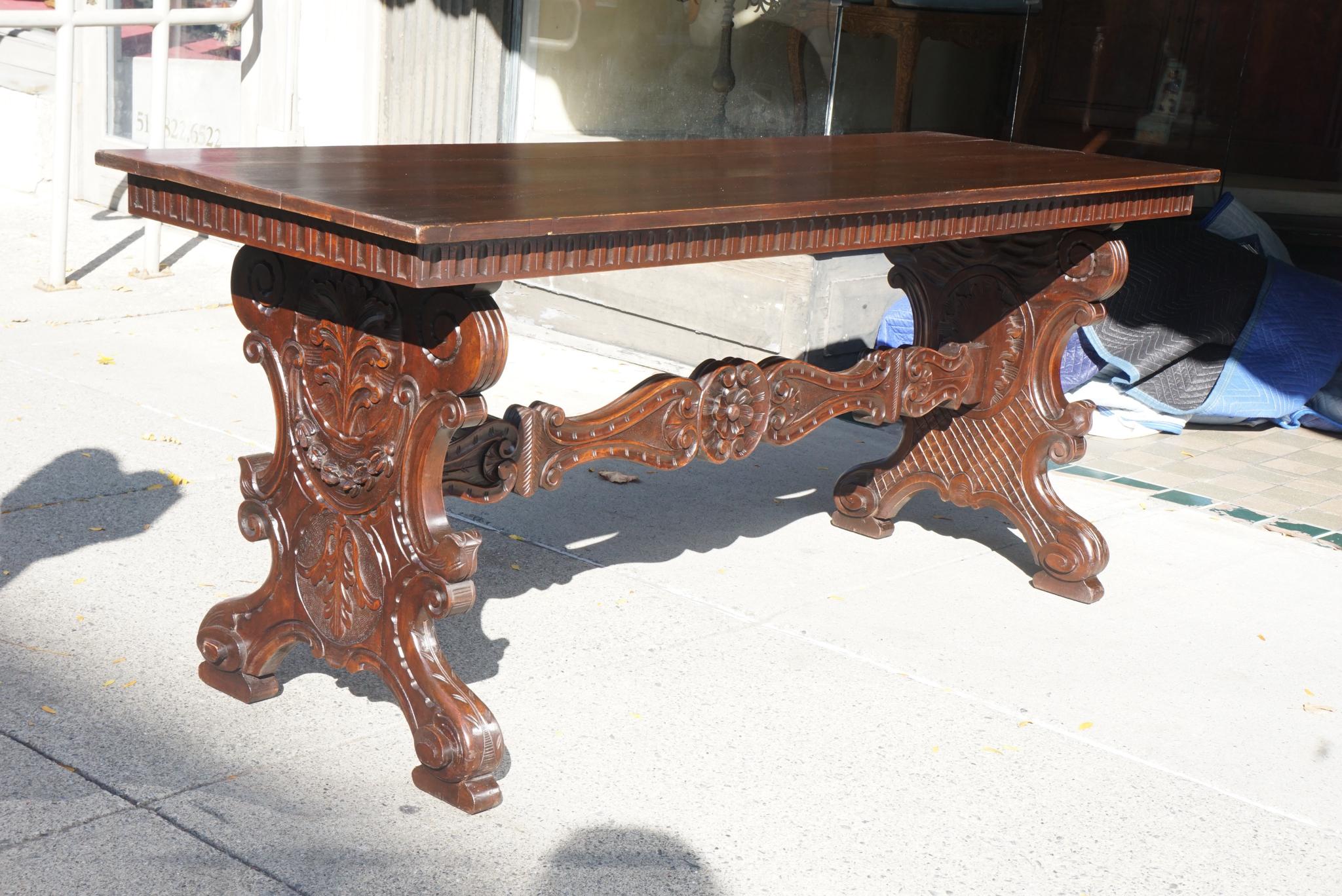 This table made in Italy circa 1900 from thick, heavily carved walnut is styled as a 17th century Florentine table. The plank board top is set upon an apron detailed with a running band of fluted carving. This then sets upon a pair of thick