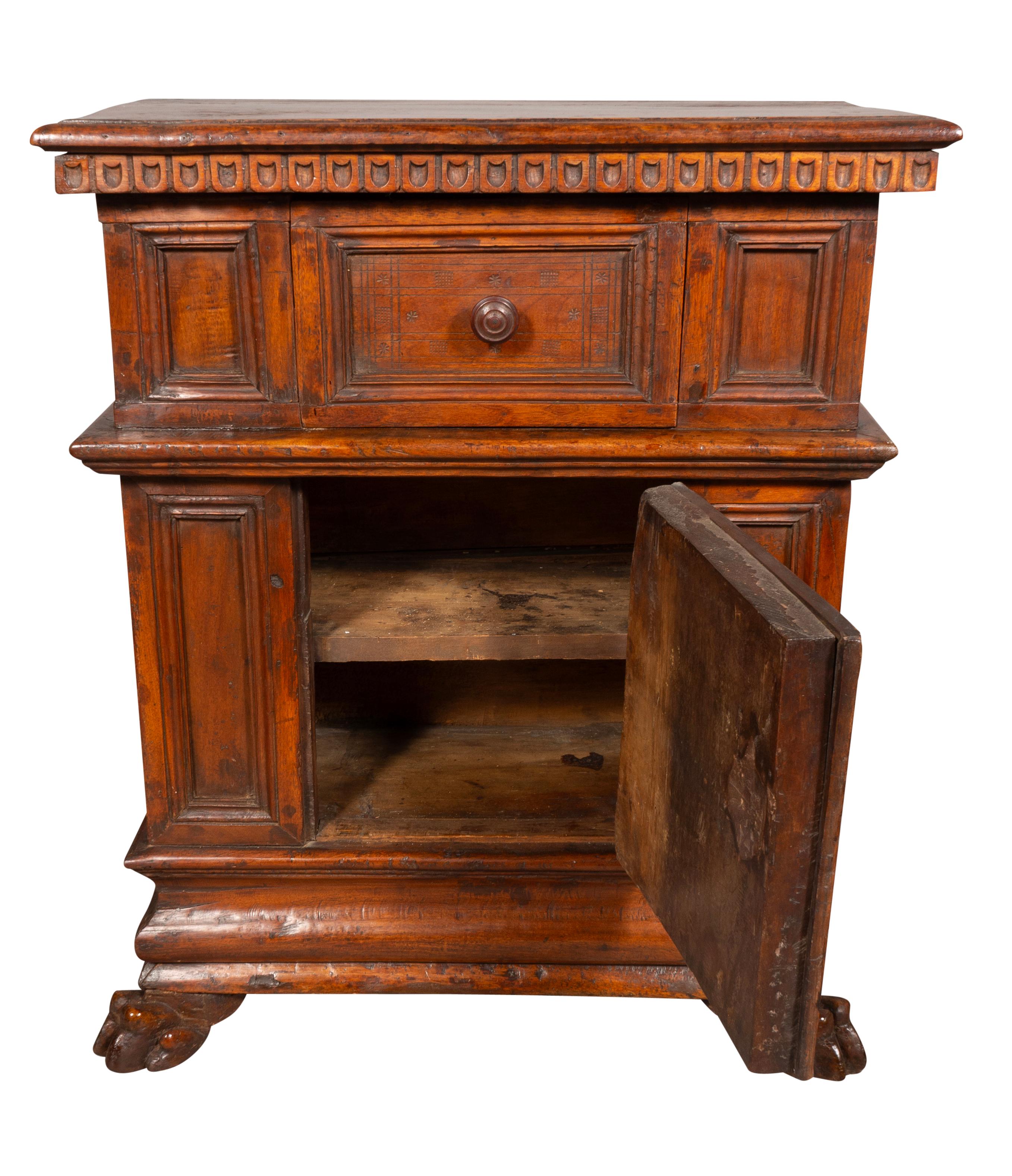 With a wonderful rich brown color and in very nice condition for its age. A rectangular top over a drawer flanked by panels over a central door with a shelf flanked by panels. Raised on paw feet. Wood knob handles.