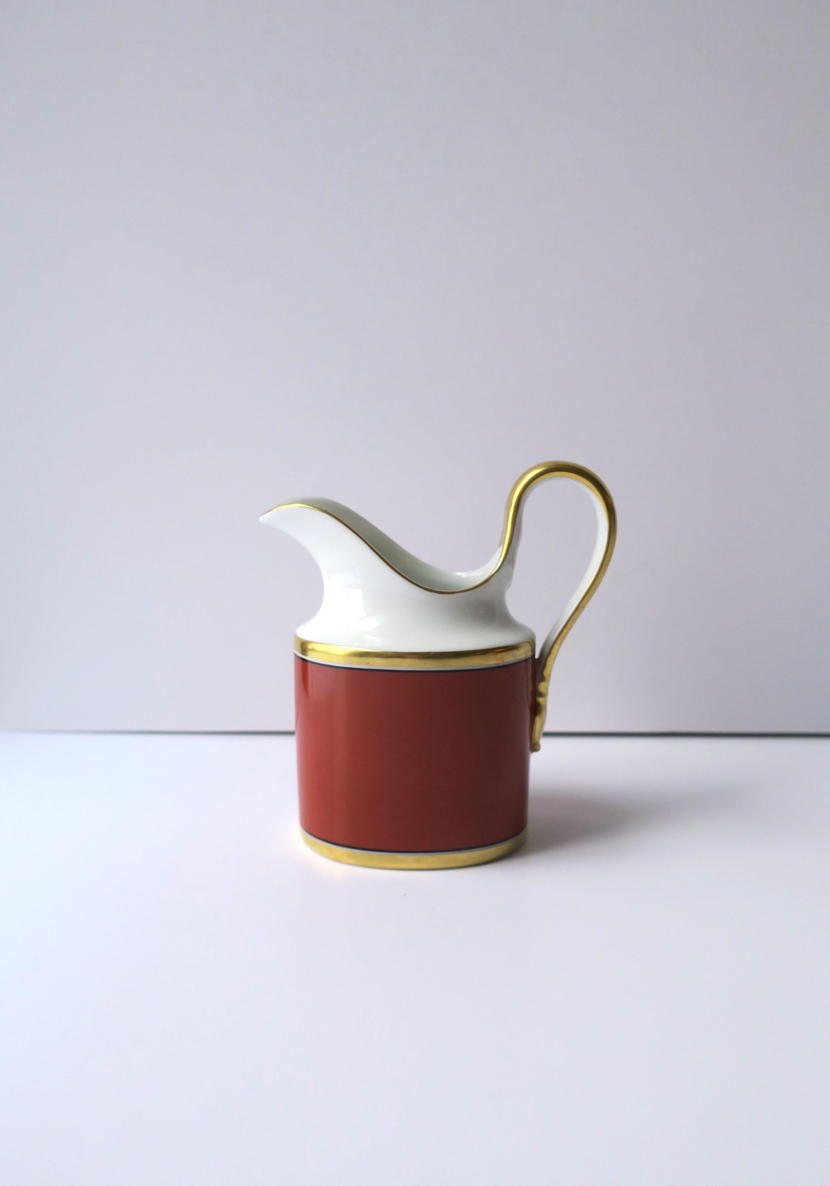 A vintage Italian Richard Ginori 'Contessa' gold and terracotta rust-red porcelain milk creamer pitcher, 1985, Italy. Piece is hand decorated with gold detail around rim, a gold band at center and base, and down handle. This 'Contessa' pattern is a
