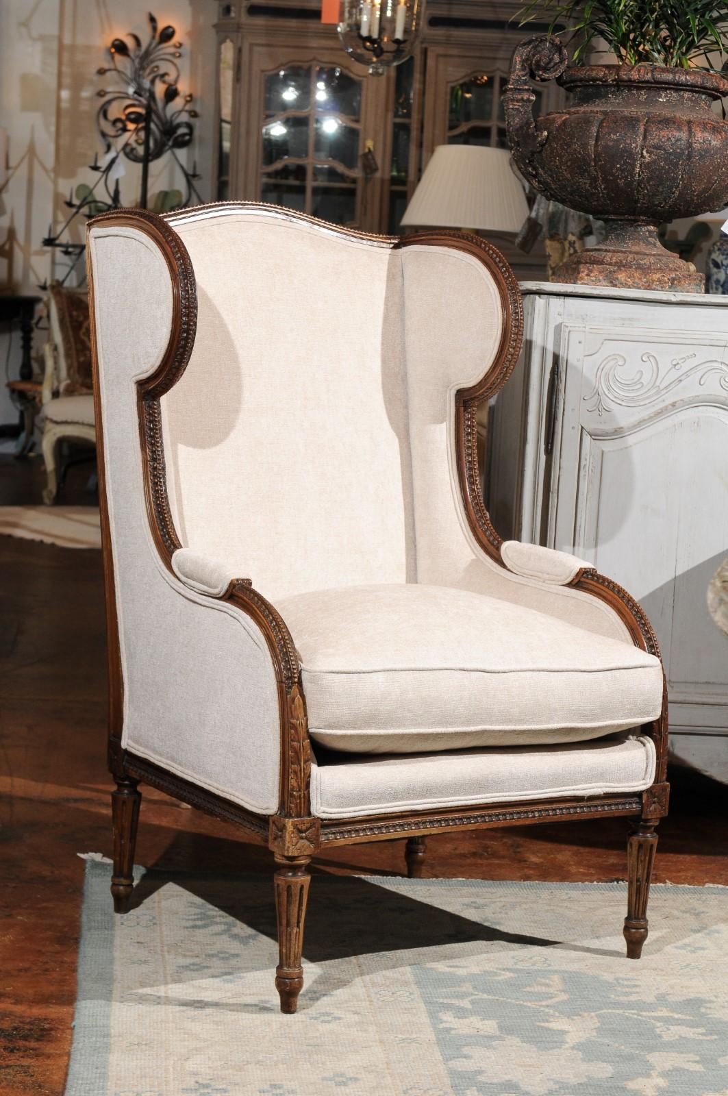 An Italian neoclassical style richly carved wooden wingback bergère chair from the late 19th century, with rais-de-cœur and beaded moldings, fluted legs and exquisite upholstery. This Italian wingback bergère features a slightly slanted rectangular