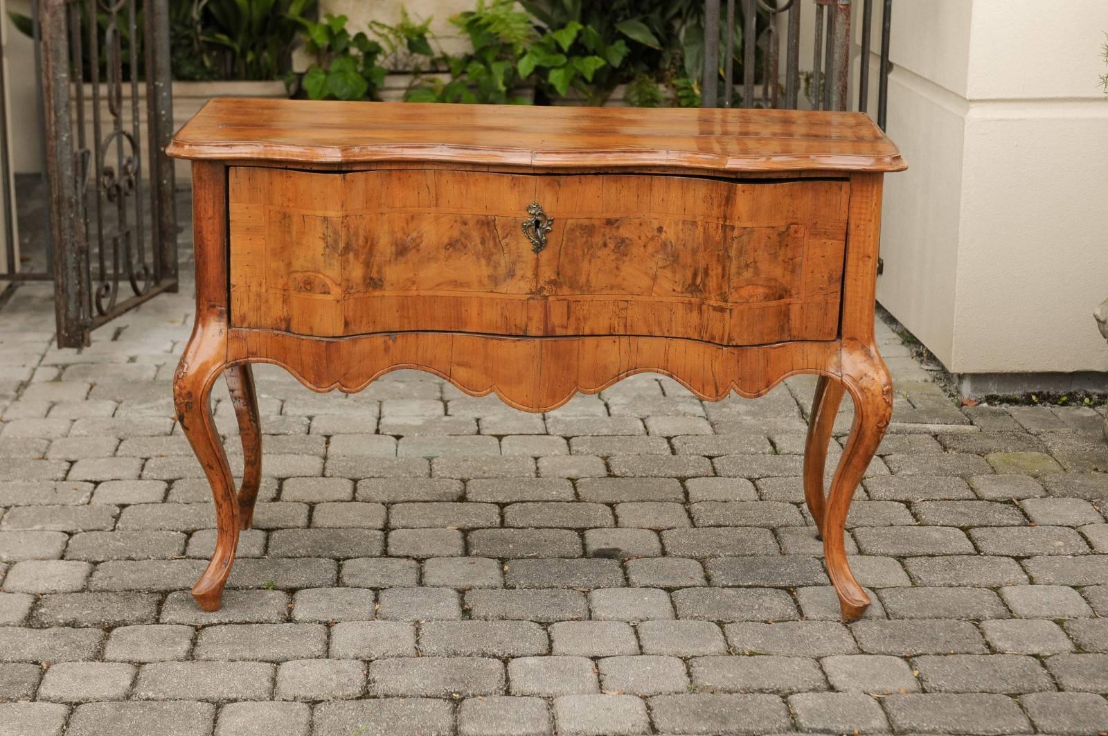 An Italian Rococo walnut single drawer commode from the early 19th century, with serpentine front and cabriole legs. Born during the second decade of the buoyant 19th century, this Italian walnut commode features a rectangular planked top with
