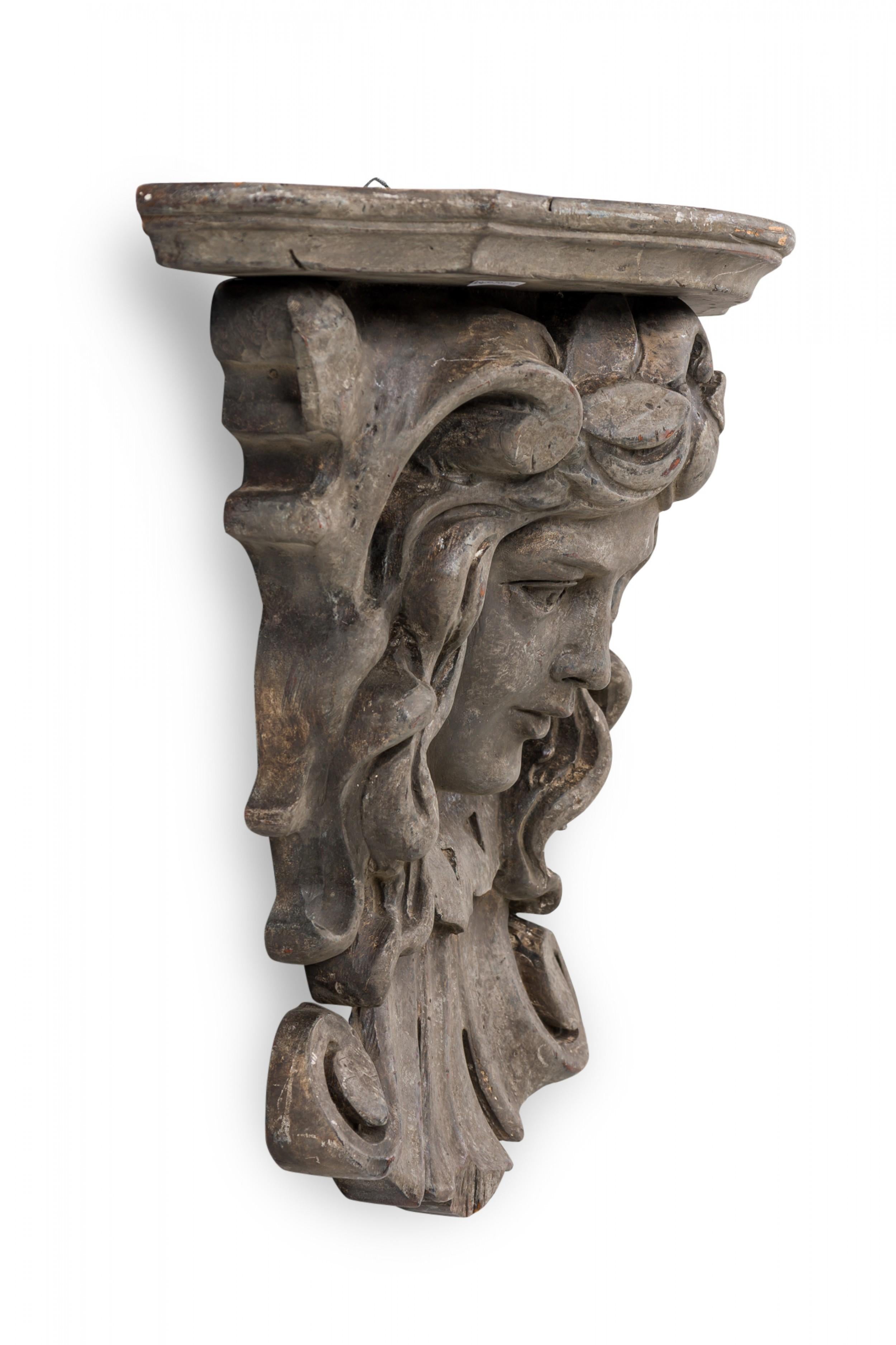 Italian Rococo-style wooden wall bracket / shelf / architectural element featuring a carved face below an upper shelf with carved and shaped beveled edge, treated with a faux bois painted finish.
