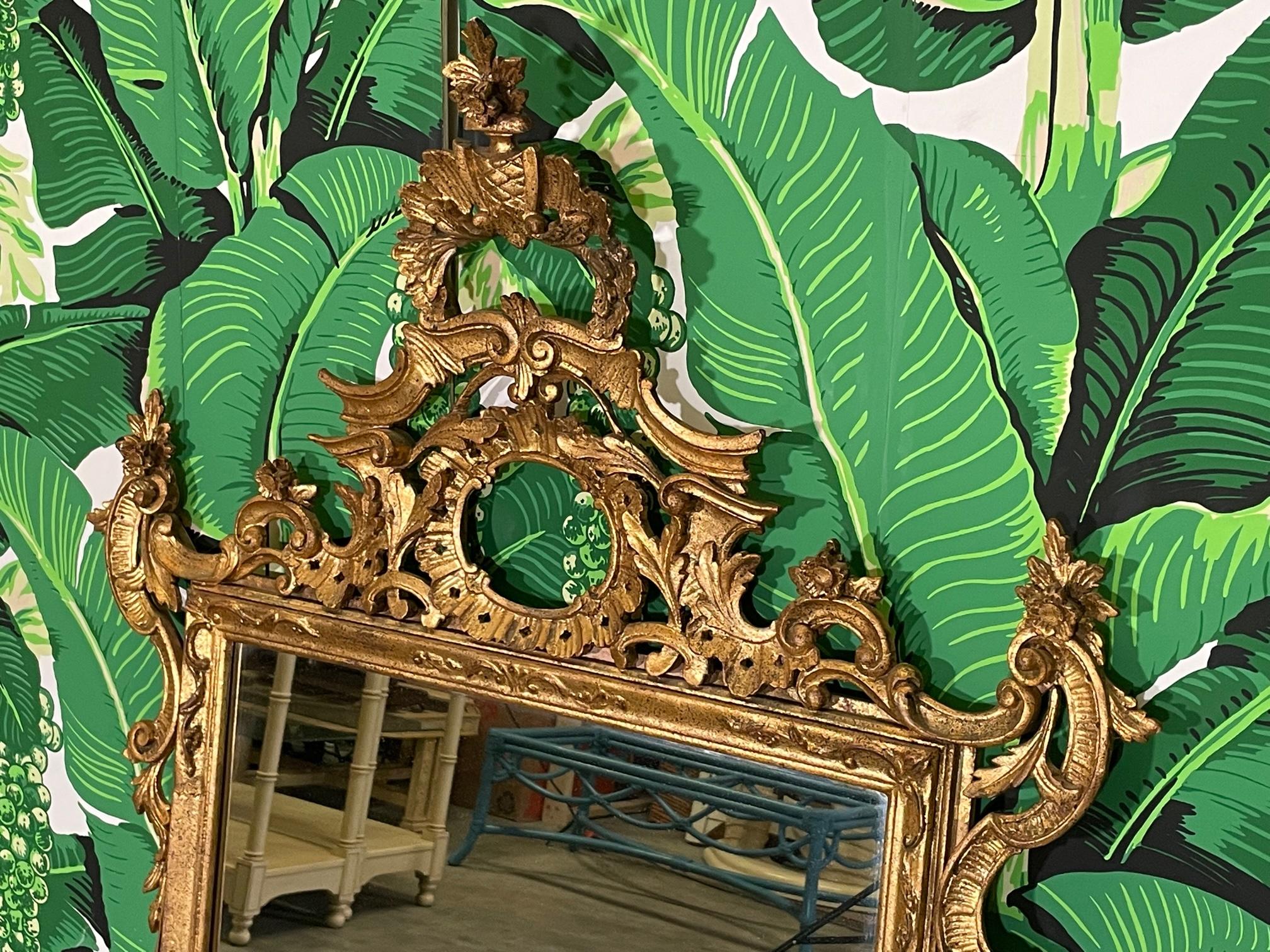 Large Rococo style wall mirror features original gold gilding and an open carved frame with flowers and scrolling acanthus leaves. Marked with Italy tag. Good condition with imperfections consistent with age. May exhibit scuffs, marks, or wear, see