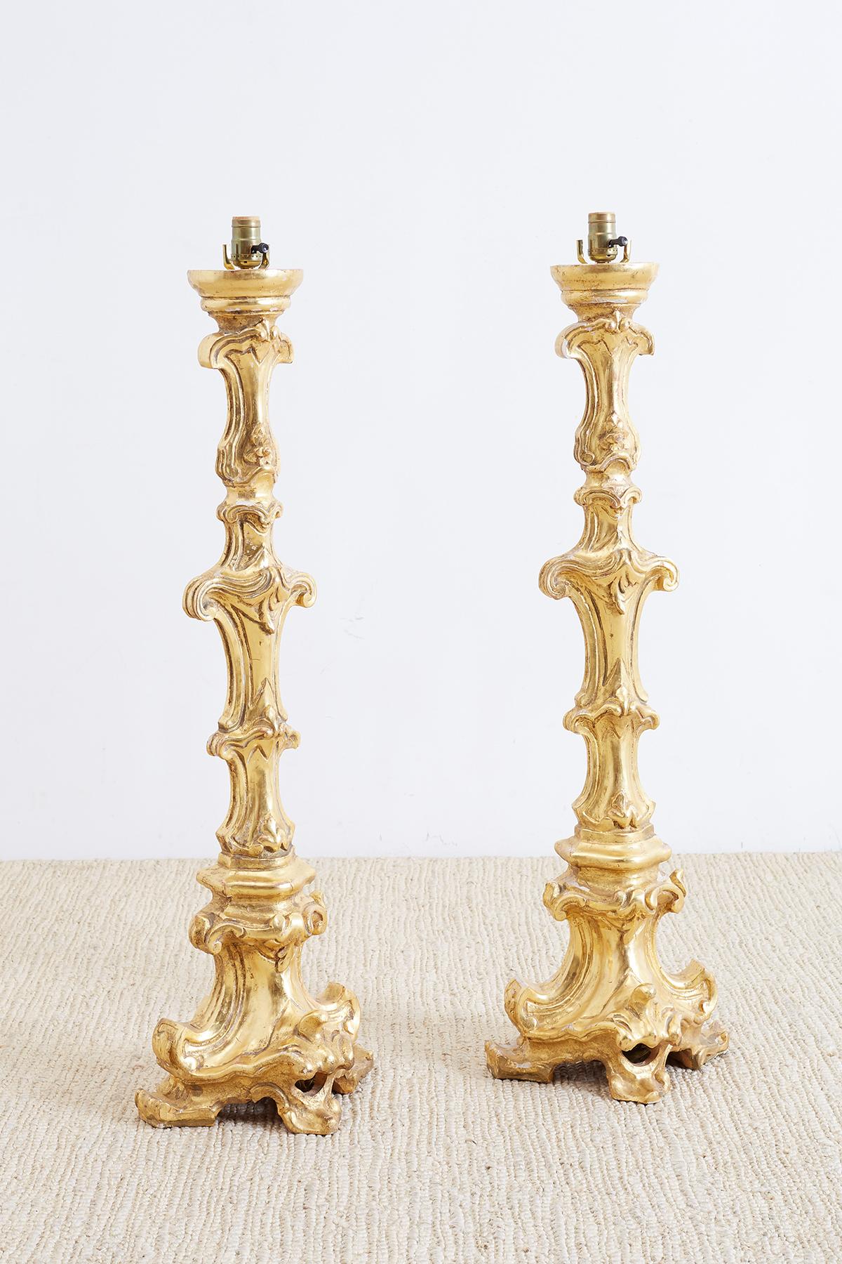 Stunning pair of Italian giltwood pricket stick or candlestick lamps made in the Rococo taste. Featuring ornately carved pricket altar sticks withs scrolls and fleur de lis decoration converted to lamps. Beautiful gold leaf finish with expected